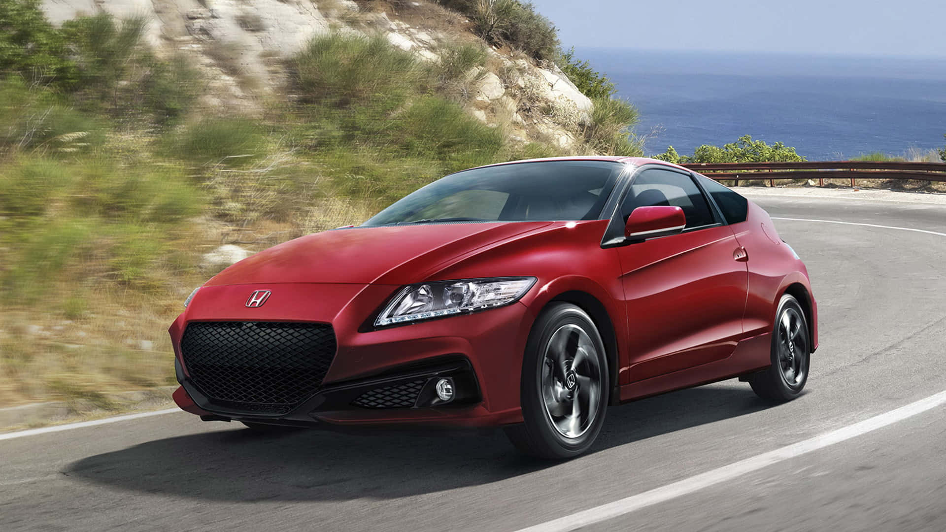 Honda Cr-z 桌布 壁紙 — 一輛鮮紅色的本田跑車沿著海岸公路飛馳，背景是模糊的綠色山丘和藍色海洋。