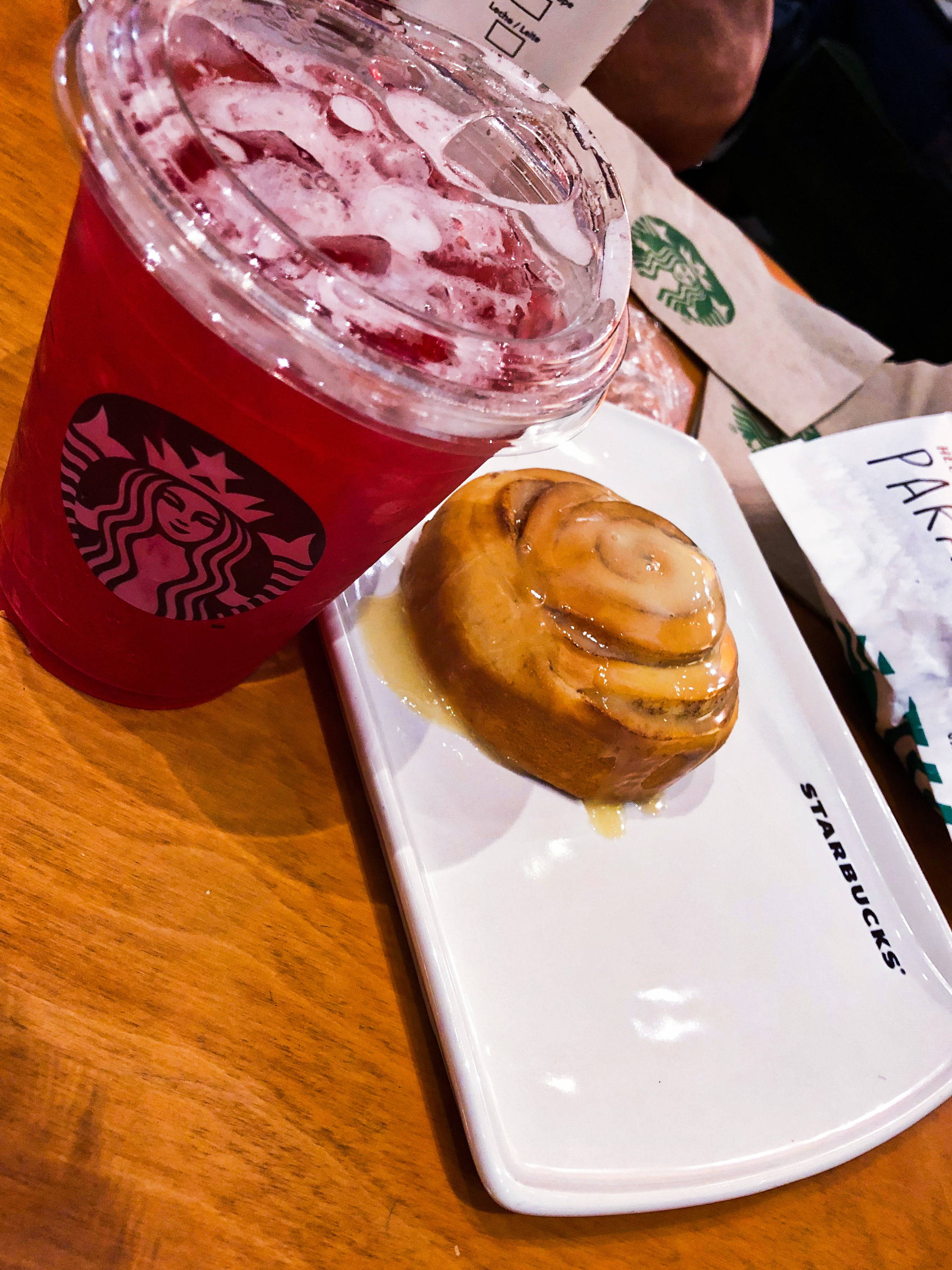 Starbucks咖啡店的白色碟子上的紅色冰凍飲品和肉桂卷。