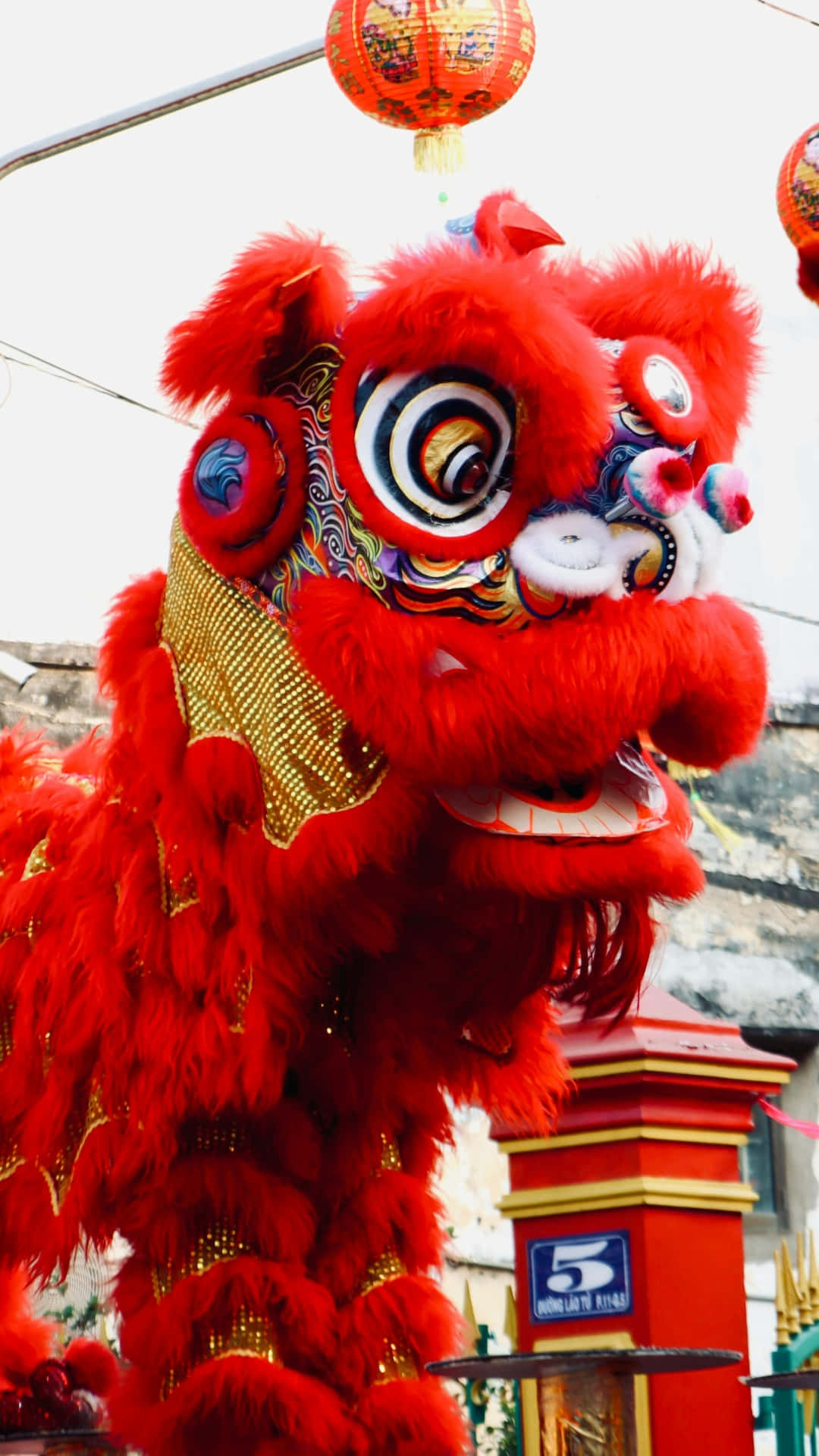  壁紙 — 一件鮮紅色的舞獅服飾，飾有精緻的金色和彩色圖案，在懸掛的燈籠下表演。
