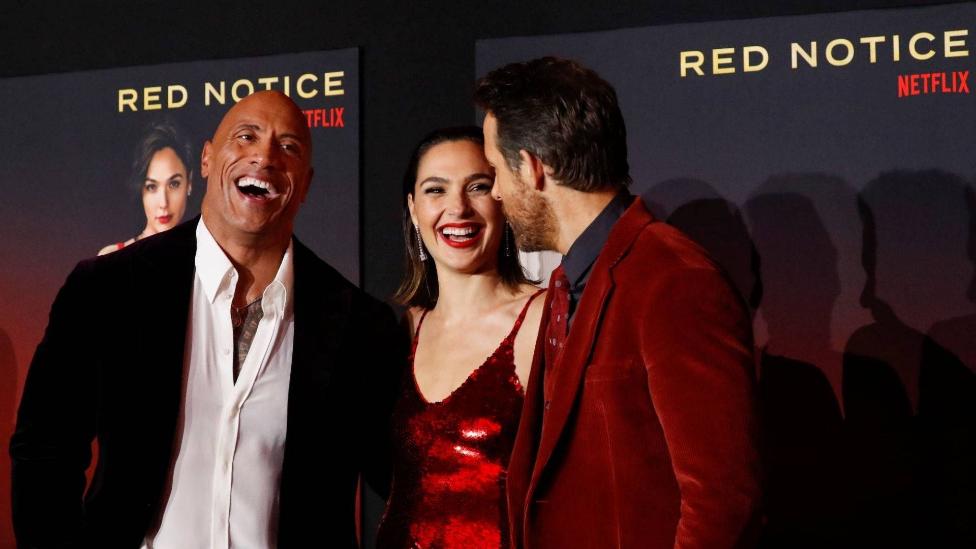 Red Notice 角色開懷大笑 壁紙 — 三位名人喺Red Notice Netflix首映禮上齊齊大笑，背後有電影海報。