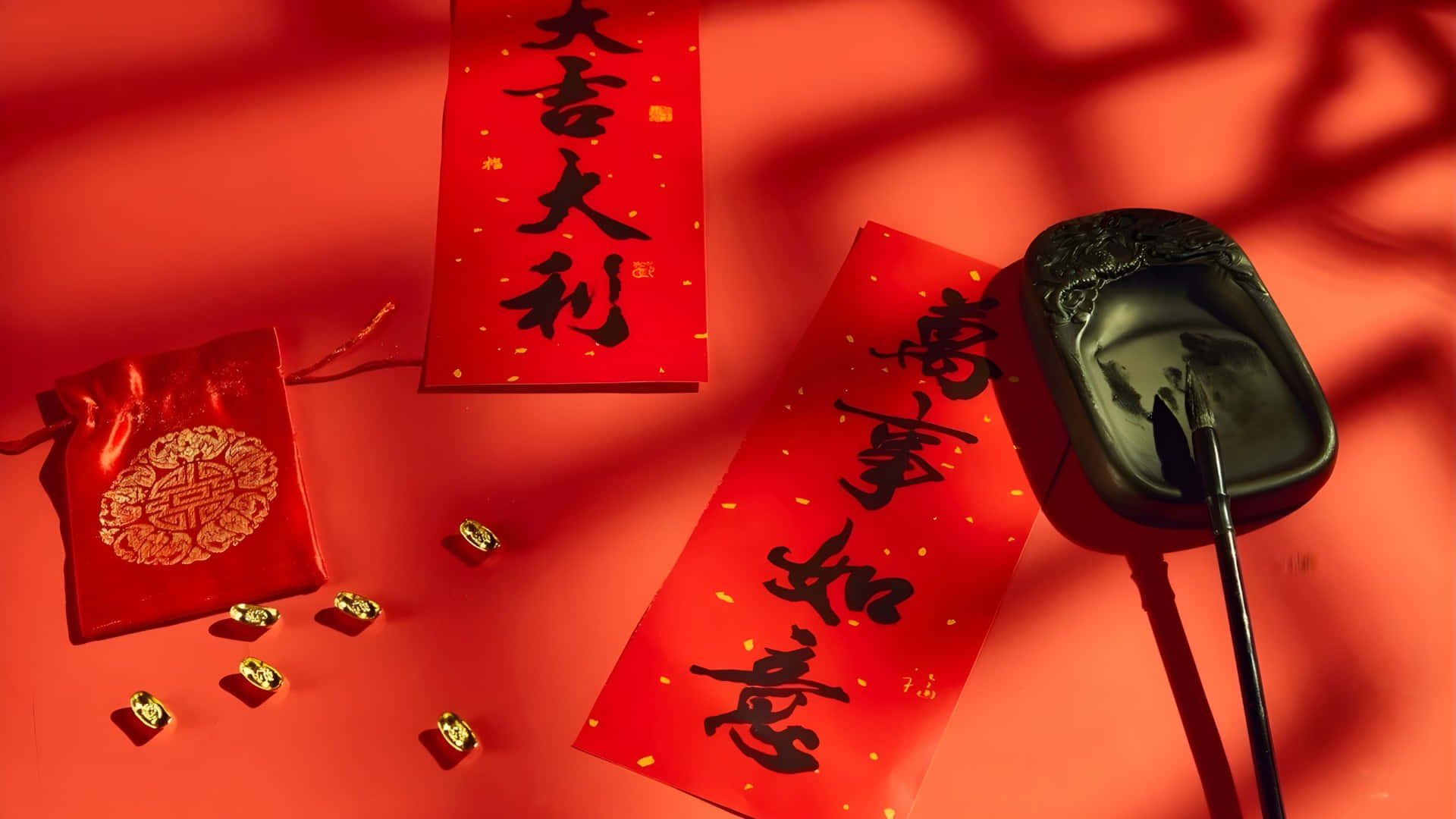  壁紙 — 紅色紙張，帶有黑色中國書法和金色點綴，沐浴在溫暖光線中，配有硯台和毛筆。