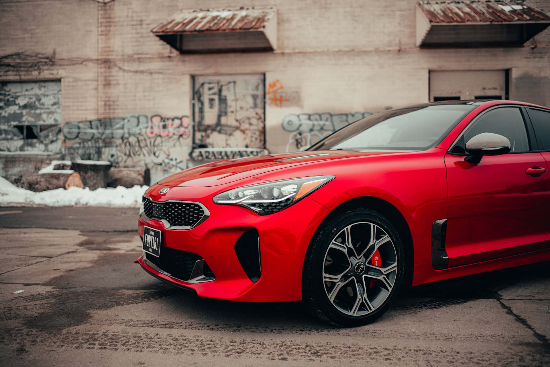 Kia Stinger 桌布 壁紙 — 一輛鮮紅色跑車停泊在佈滿塗鴉的市區牆前，地上有積雪。