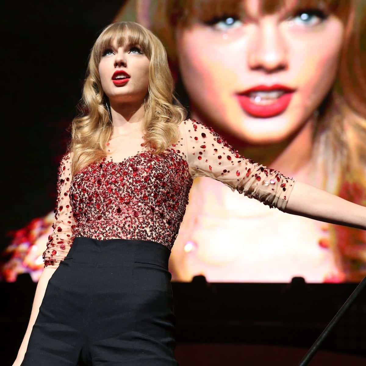 Taylor Swift 在舞台上現場表演，身穿紅色亮片上衣和黑色褲子。