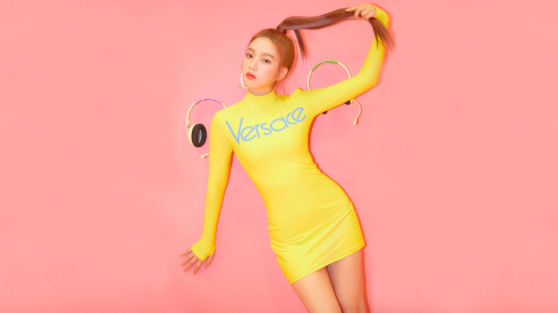 身穿黃色 Versace 連衣裙的女性在粉色背景下戴著耳機擺姿勢
