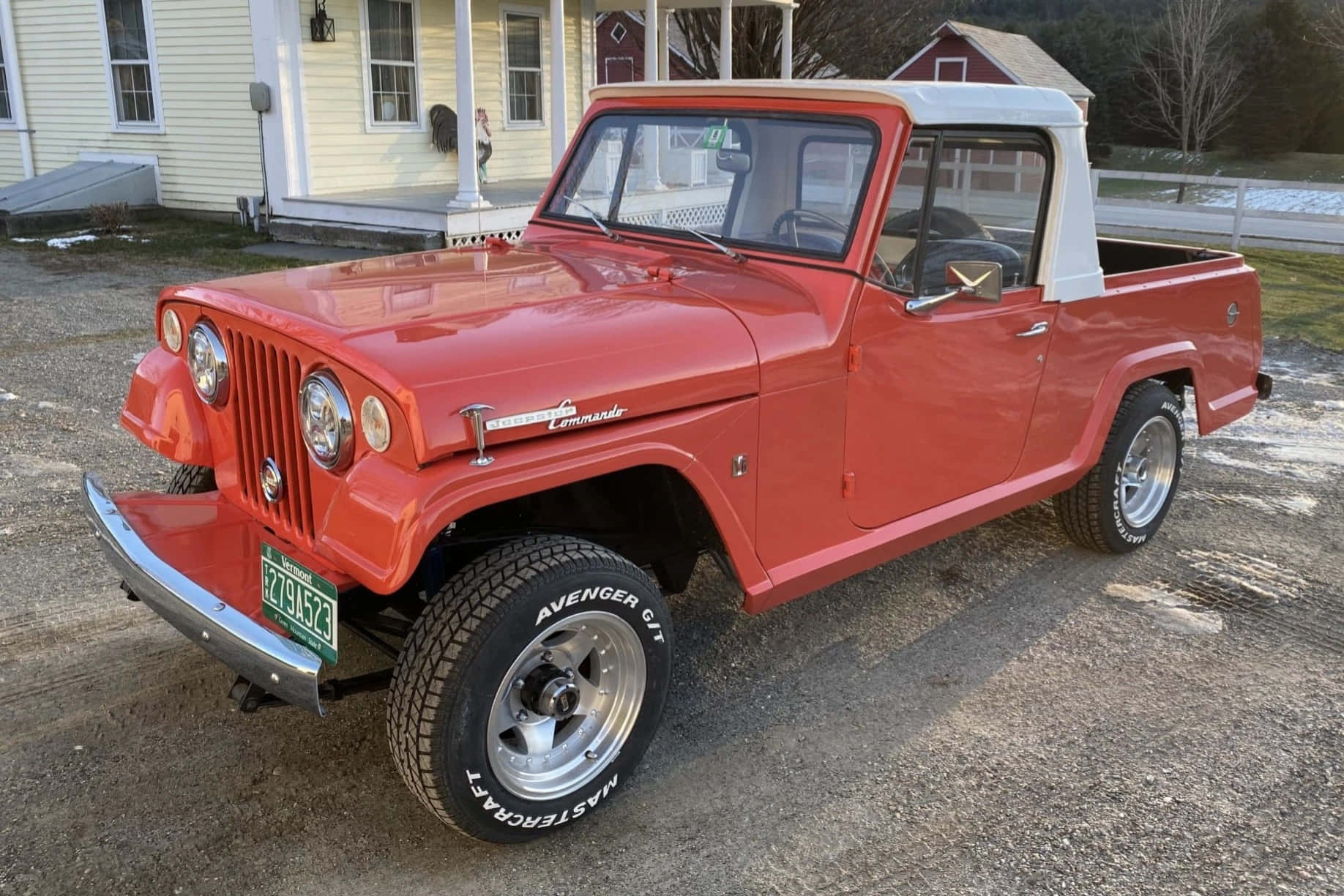 Jeepster 桌布 壁紙 — 一輛鮮紅色的復古Jeep Commando皮卡車停在碎石路上，前面是一棟黃色房子，附近有雪堆。