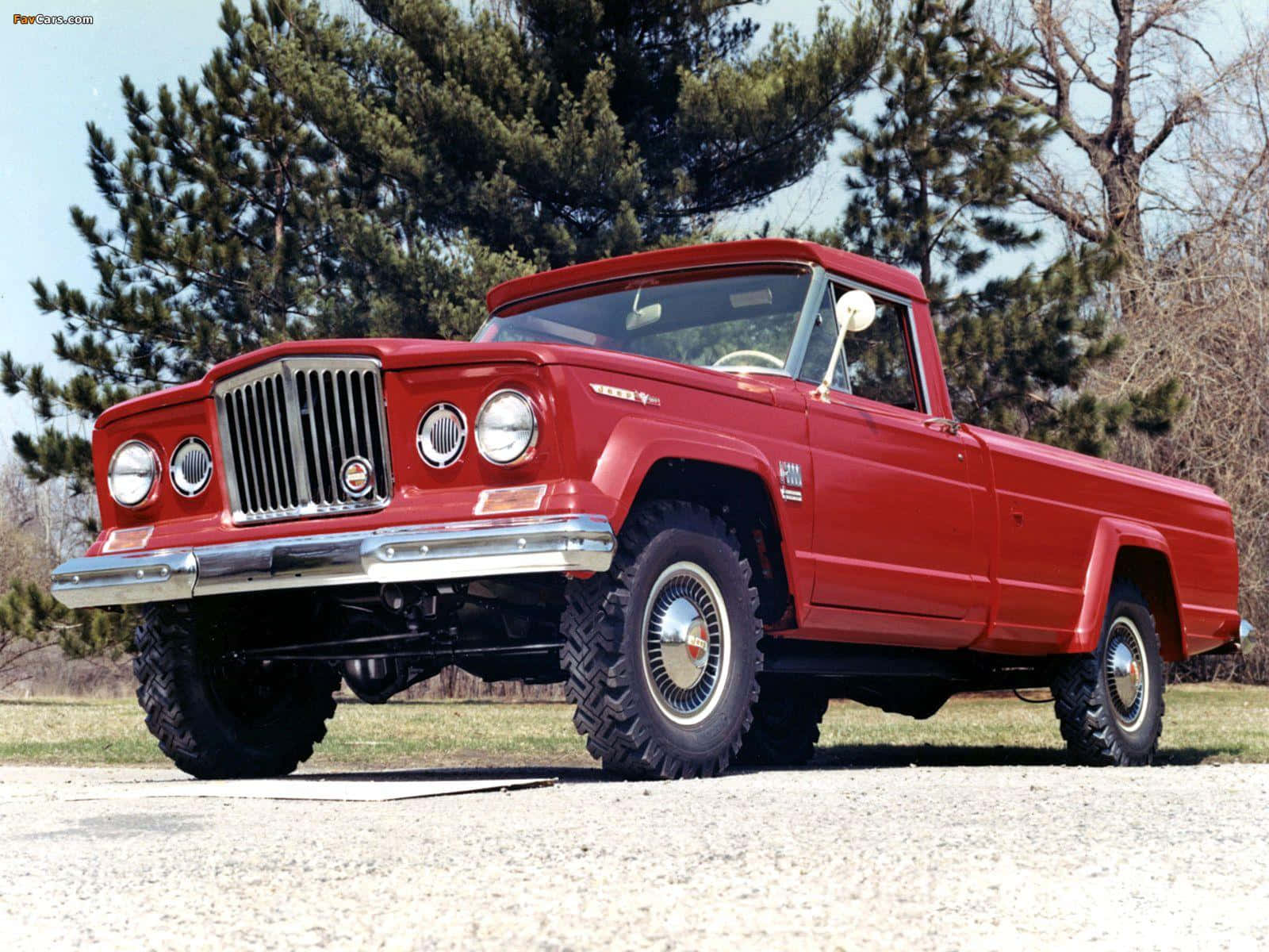 Jeep Gladiator 桌布 壁紙 — 一輛鮮紅色的復古Jeep皮卡車，帶有鍍鉻裝飾和大輪胎，自豪地停在碎石地上，旁邊是常綠樹，天空晴朗。