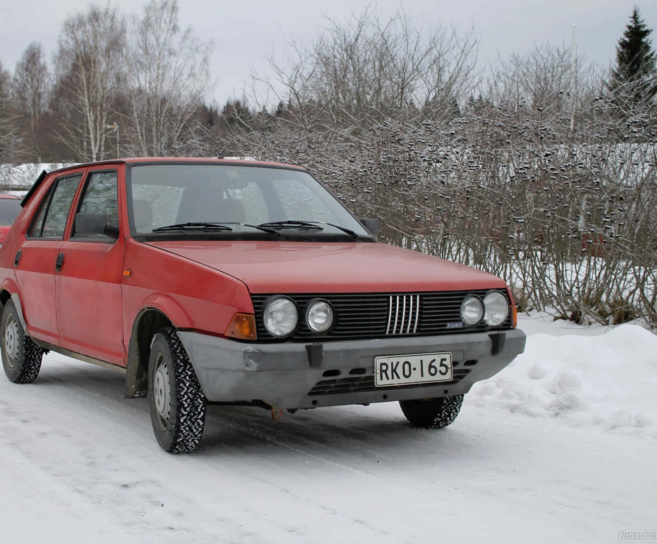 Fiat Ritmo 桌布 壁紙 — 一輛紅色復古轎車，輪胎上覆蓋著雪，停在雪地路邊，周圍是光禿禿的冬季樹木。