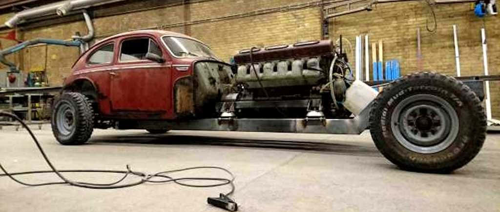 Volvo Pv544 桌布 壁紙 — 一輛紅色復古福士甲蟲車，配備巨大的V8引擎和超大輪胎，放置在雜亂車庫的金屬框架上。