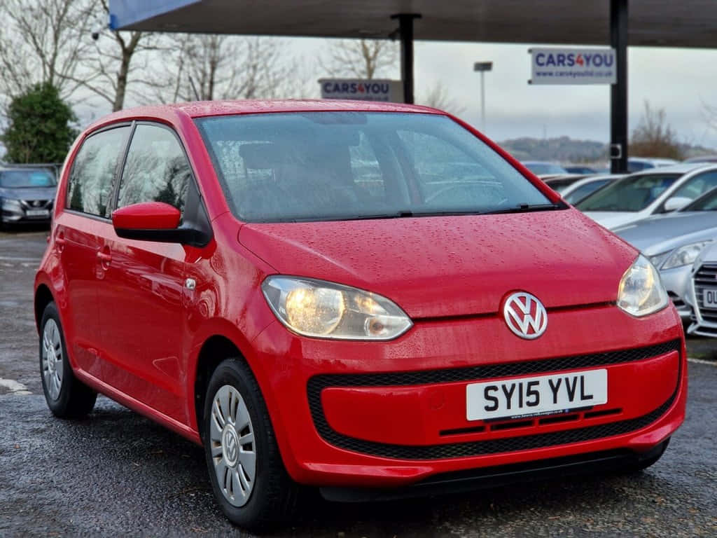  壁紙 — 一輛鮮紅色的Volkswagen up!在陰天潮濕的汽車經銷商場地中閃閃發光，附近有其他車輛。