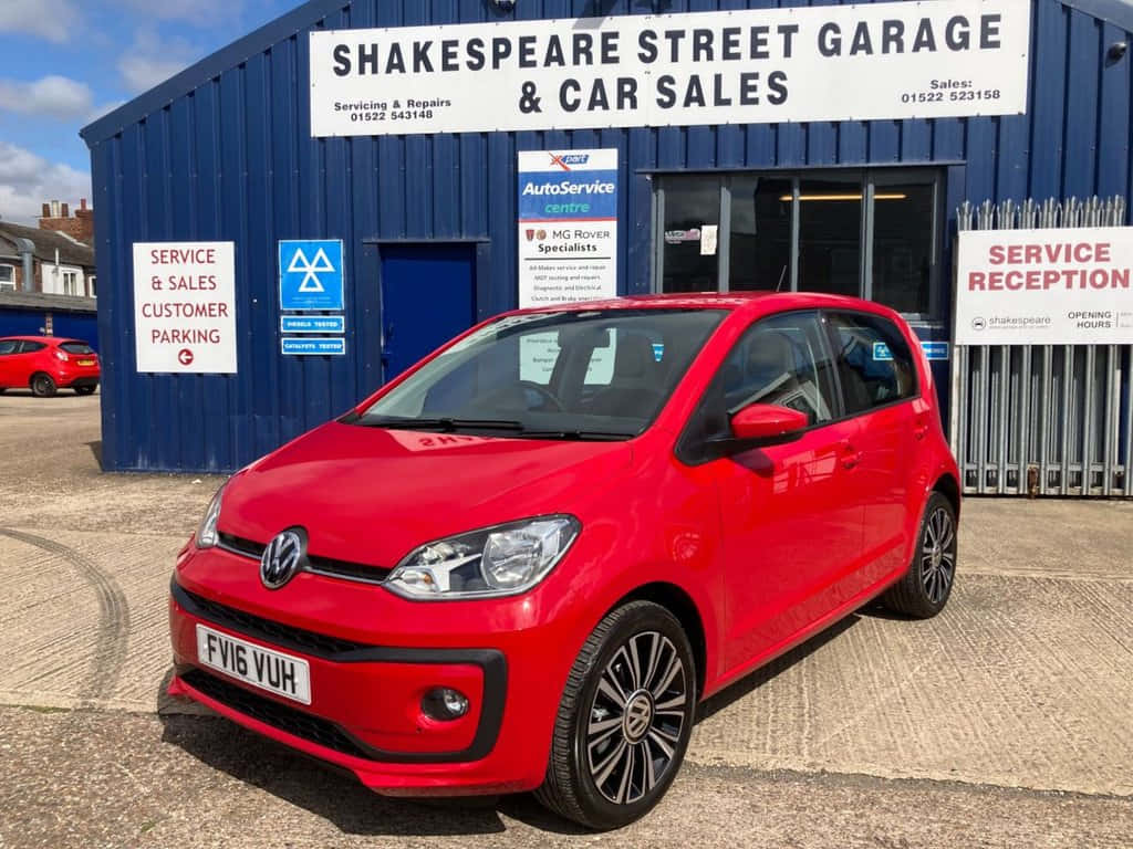 壁紙 — 一輛鮮紅色的Volkswagen up!停泊在藍色汽車車庫前，天空清澈湛藍。