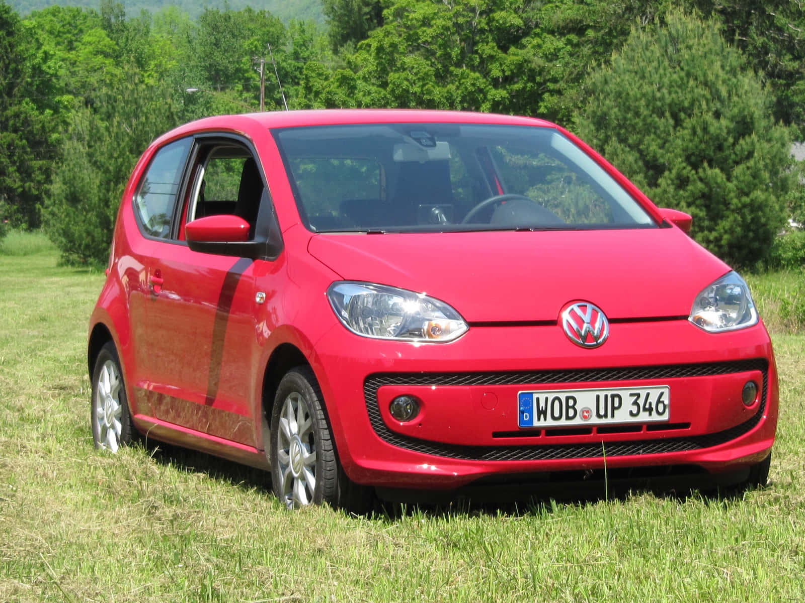  壁紙 — 一輛鮮紅色的Volkswagen up停泊在陽光明媚的草地上，背景是茂密的綠樹。