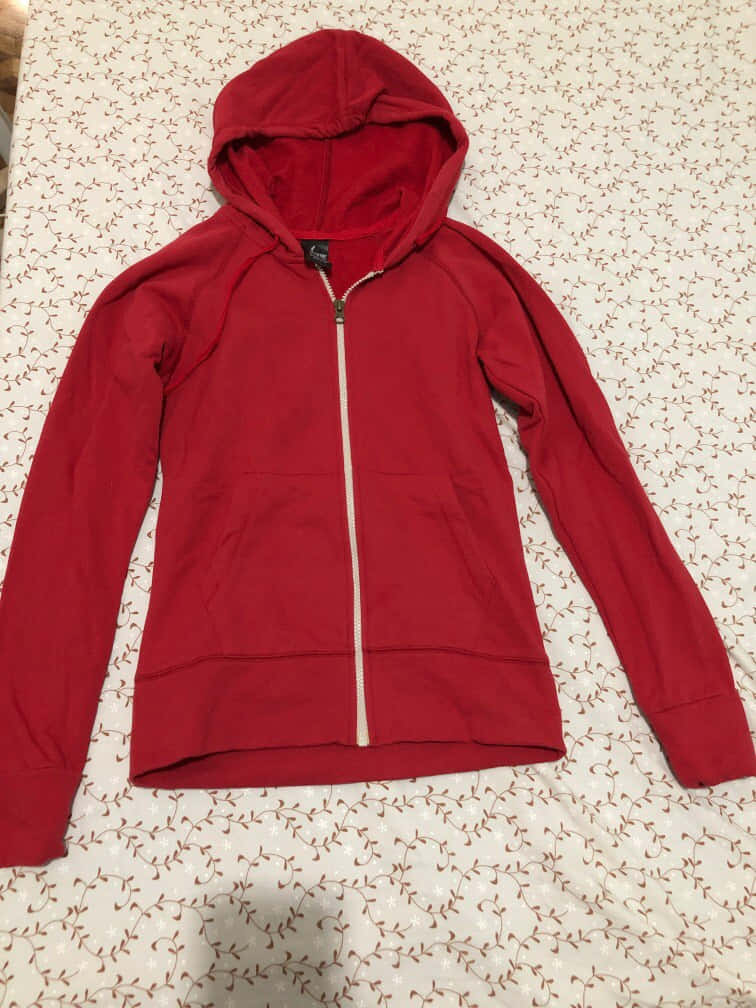 Red Hoodie 桌布 壁紙 — 一件鮮紅色拉鍊連帽衛衣，配有白色拉鍊，平放在有圖案的床罩上。