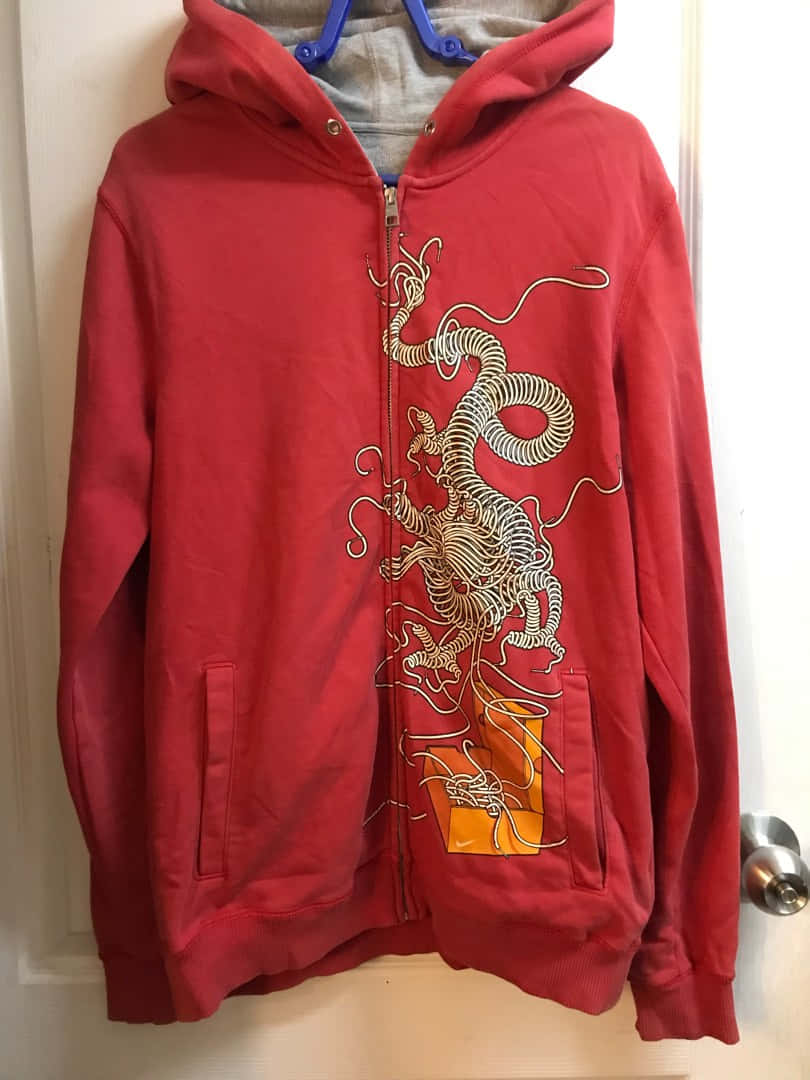Red Hoodie 桌布 壁紙 — 一件紅色拉鍊連帽衛衣，上面有精細的白色龍圖案，掛在藍色衣架上，背景是白色門。