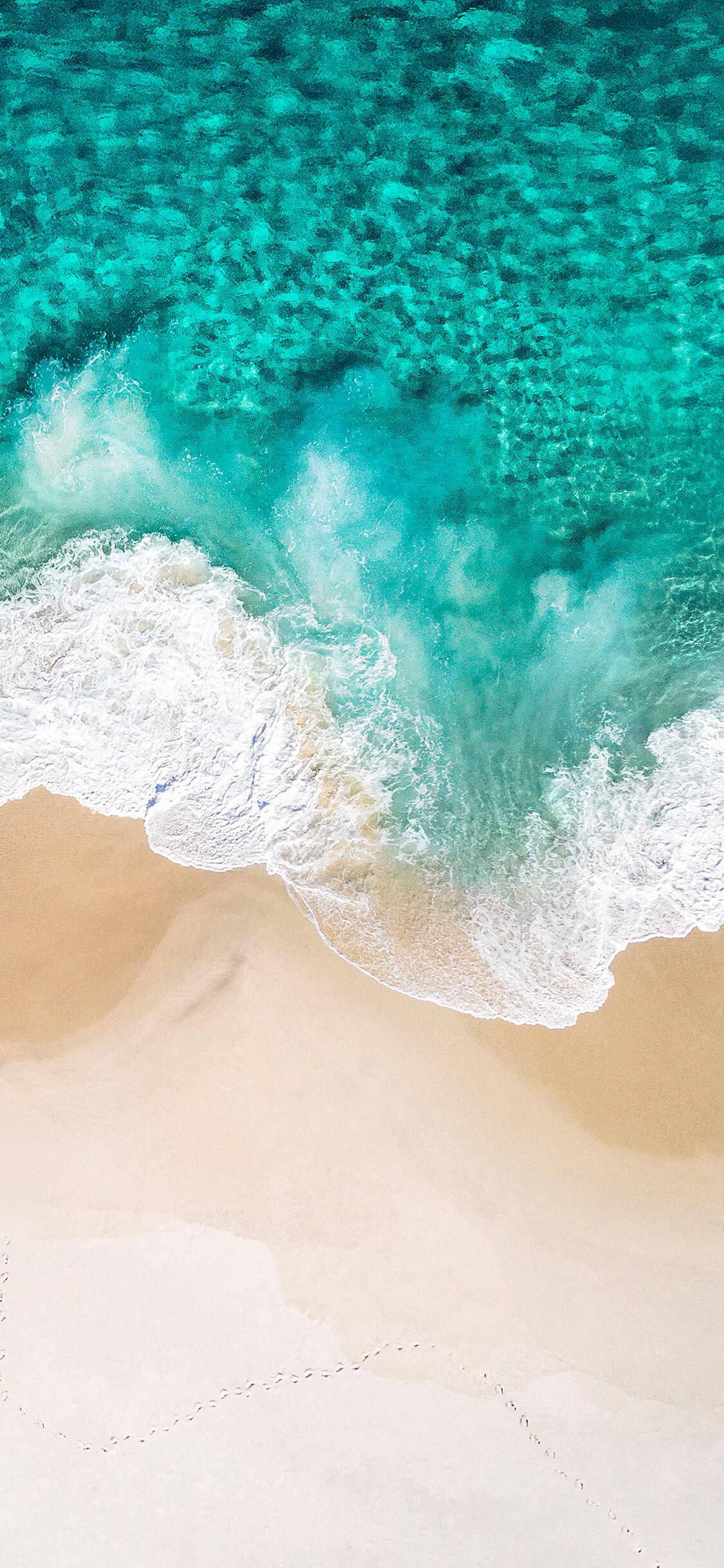Redmi 9 海浪 壁紙 — 從空中俯瞰，碧綠色的海浪拍打著純淨的沙灘，沙灘上可見腳印。