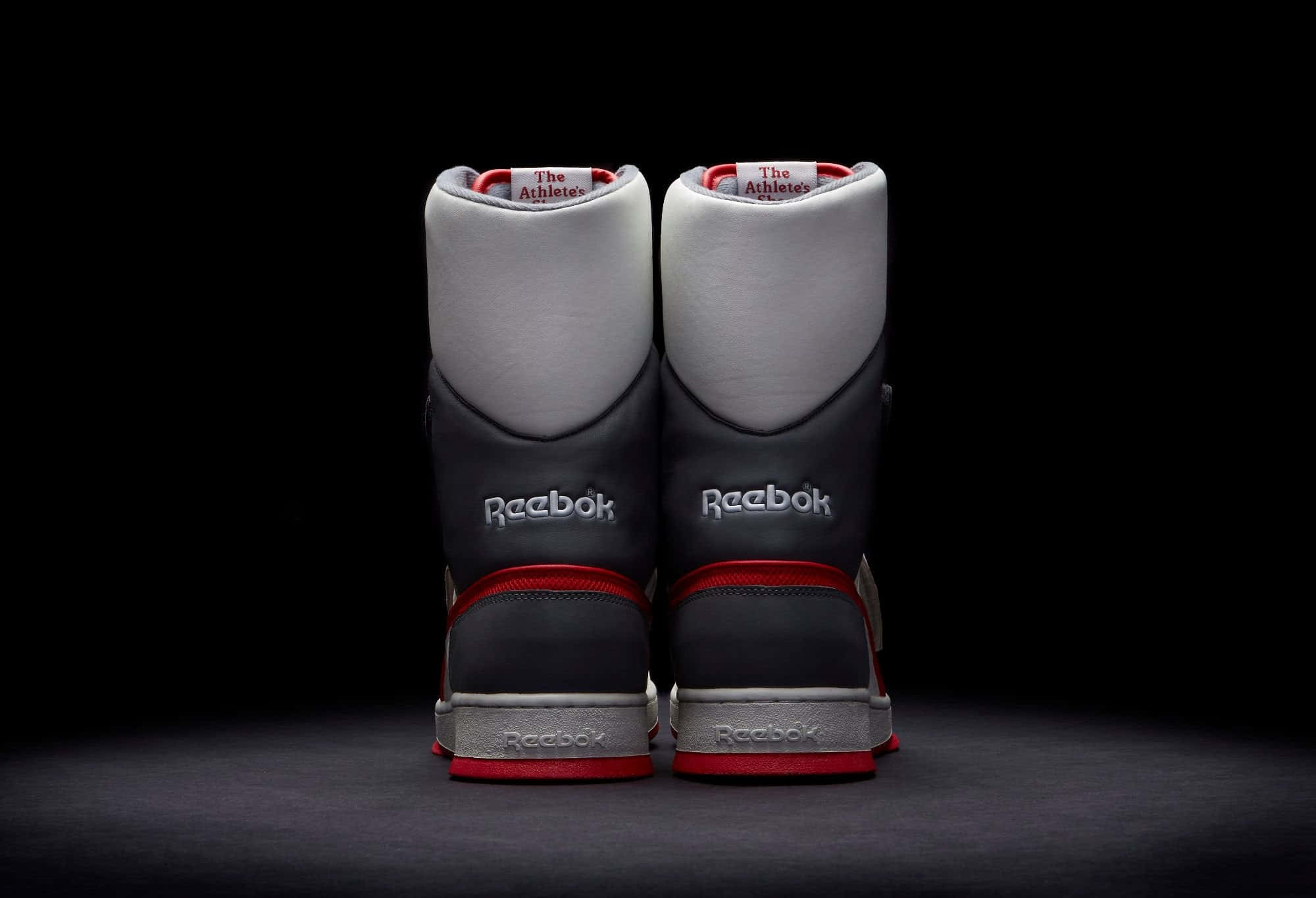 高強度時尚風格 – Reebok 壁紙 — 一對Reebok運動鞋從後面觀看，背景為純黑色，帶有戲劇性的聚光燈。