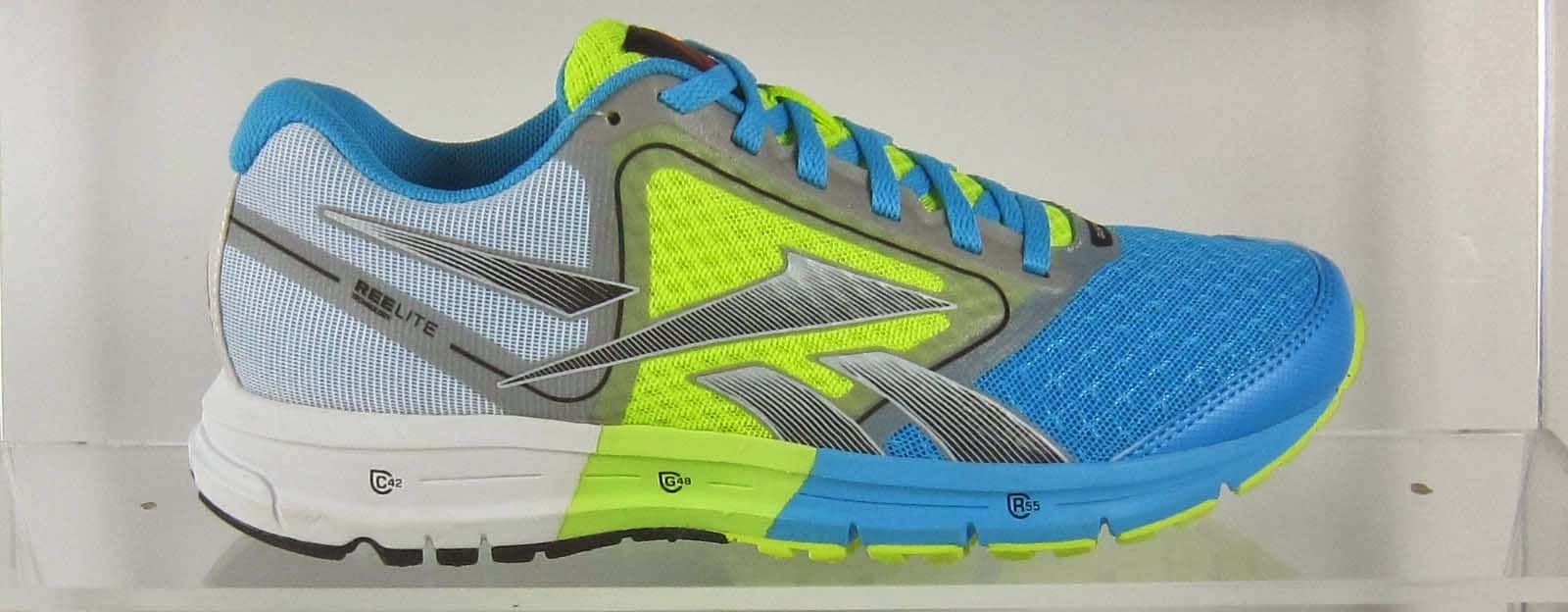以Reebok征服每一天！ 壁紙 — 一雙充滿活力的藍色和螢光黃色跑鞋，帶有銀色點綴，展示在透明支架上，背景為純白色。