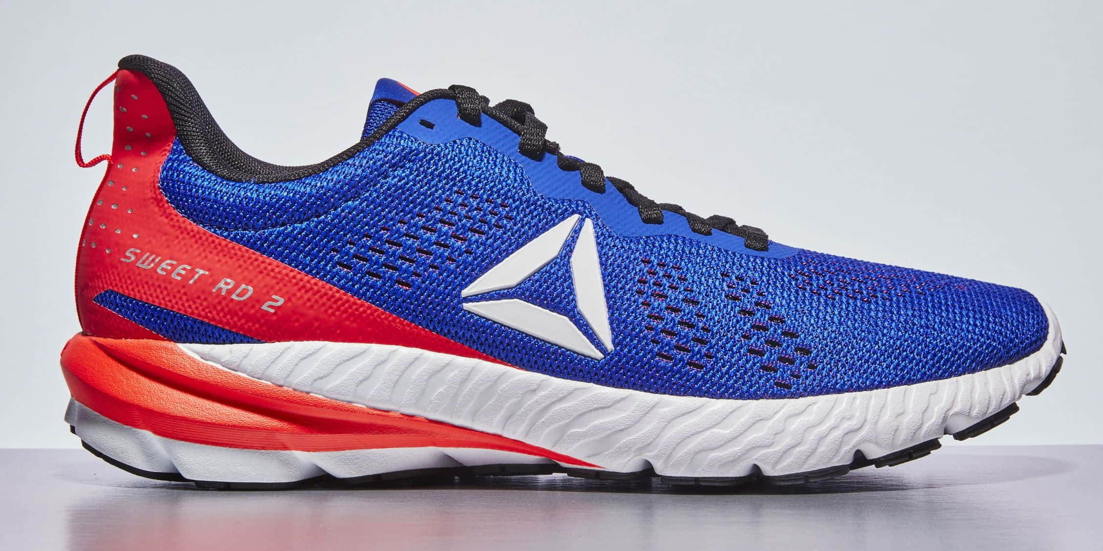 穿上Reebok，邁向成功 壁紙 — 充滿活力的藍色和紅色 Reebok 跑鞋，白色鞋底和黑色鞋帶，在工作室燈光下展示。
