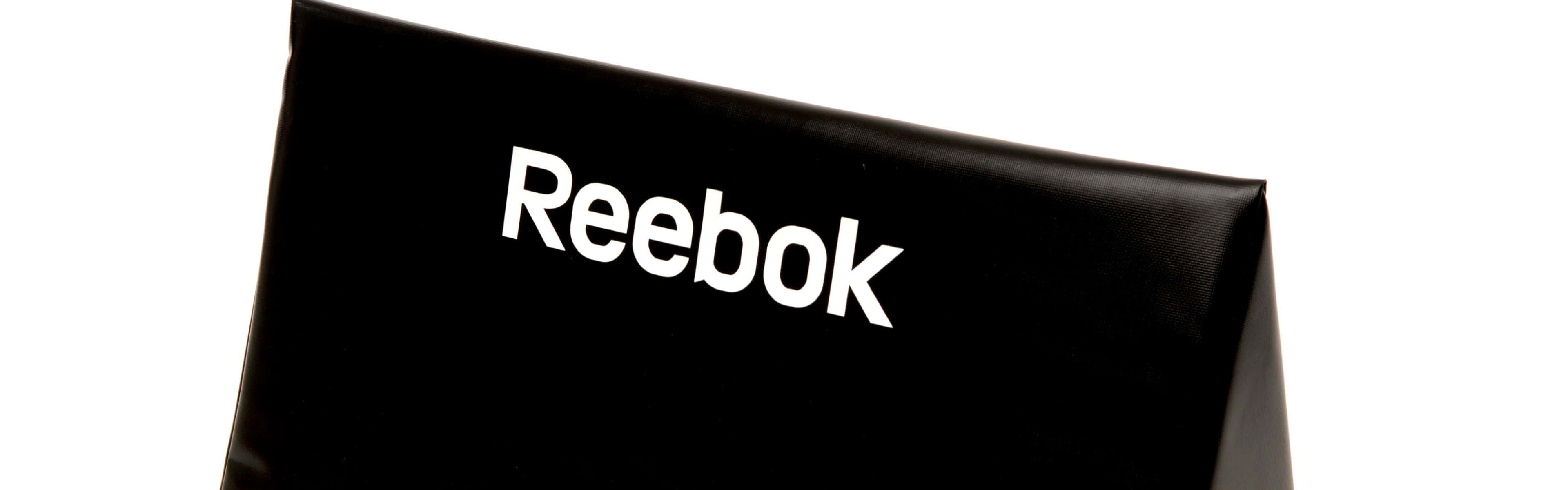 Reebok，為生活打造完美體態 壁紙 — 黑色 Reebok 品牌拳擊靶墊的特寫，帶有粗體白色標誌，背景為純白色。