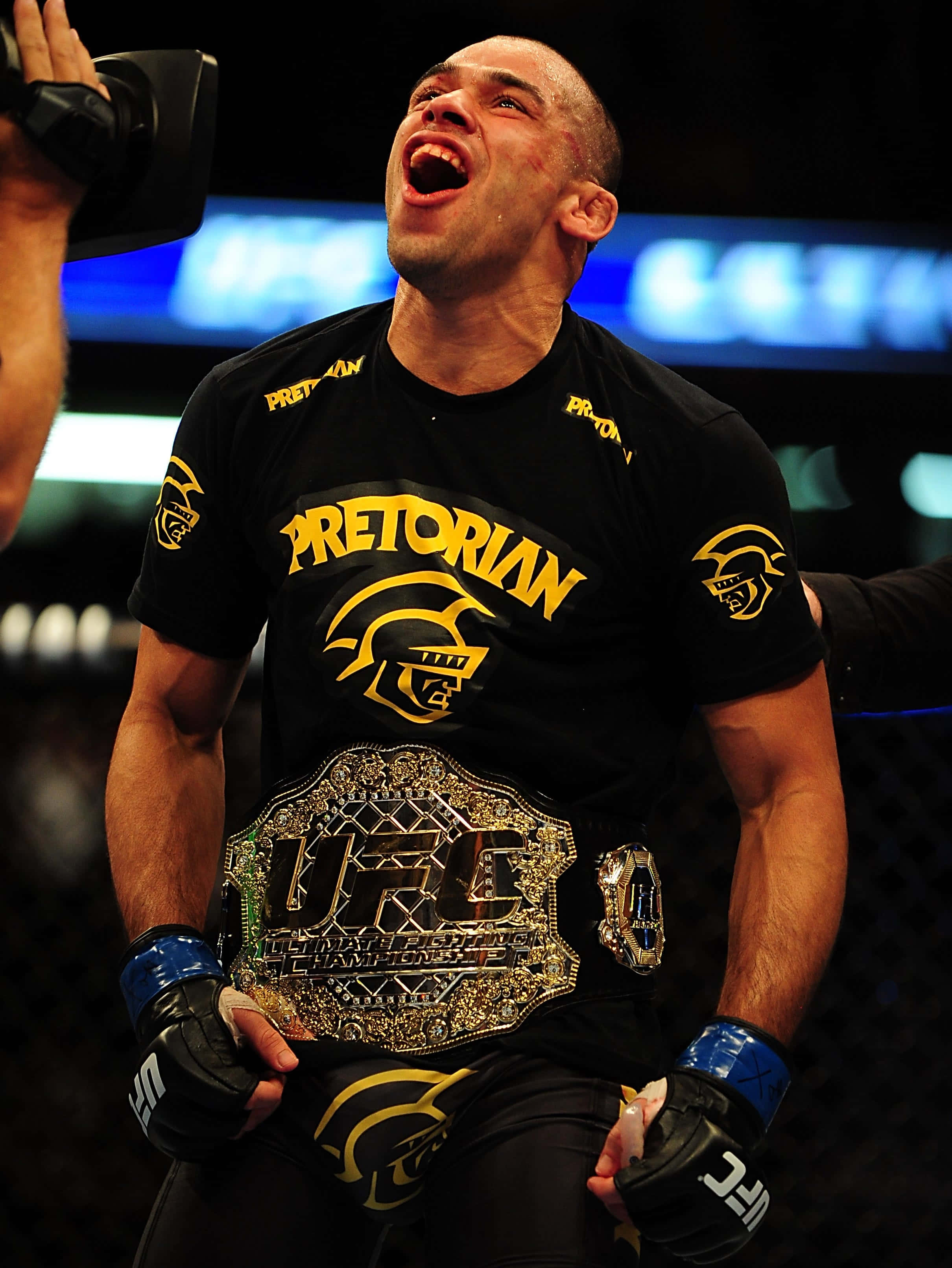 Renan Barão擊敗Wineland奪冠 壁紙 — 一位身穿黑色Pretorian襯衫的UFC勝利戰士，高舉冠軍腰帶，發出勝利的怒吼。