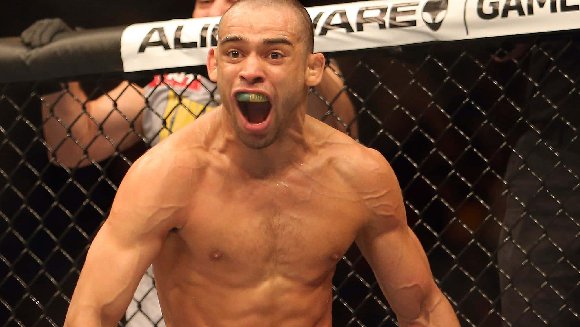 Renan Barão於UFC 173賽事中勝利驚喜 壁紙 — 一名赤裸上身的肌肉鬥士在籠內勝利咆哮，籠上可見'Alienware'品牌標誌。