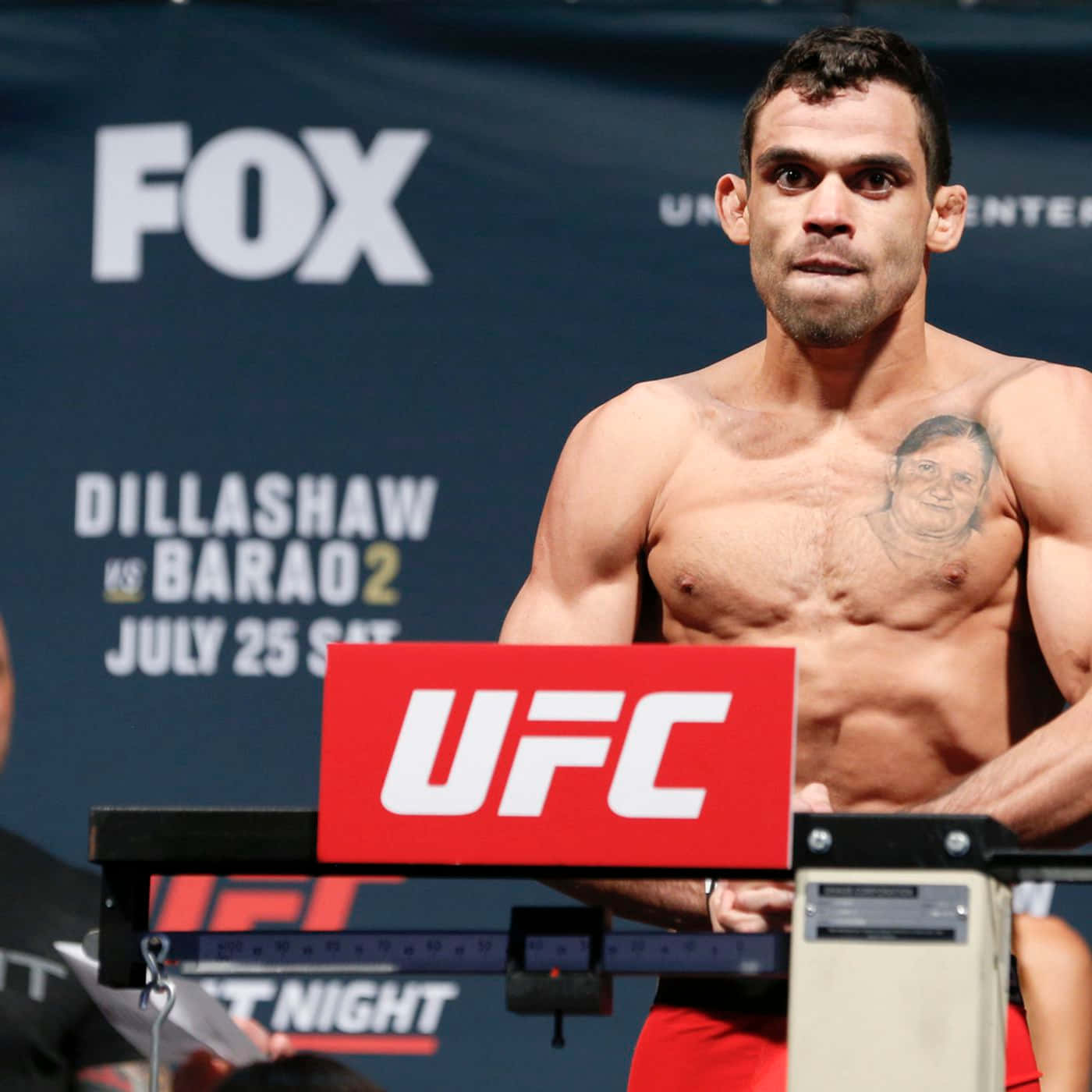 Renan Barão與TJ Dillashaw賽前稱重 壁紙 — 一位肌肉發達的UFC拳手在FOX廣播背景的稱重活動中赤裸上身站在體重磅上。