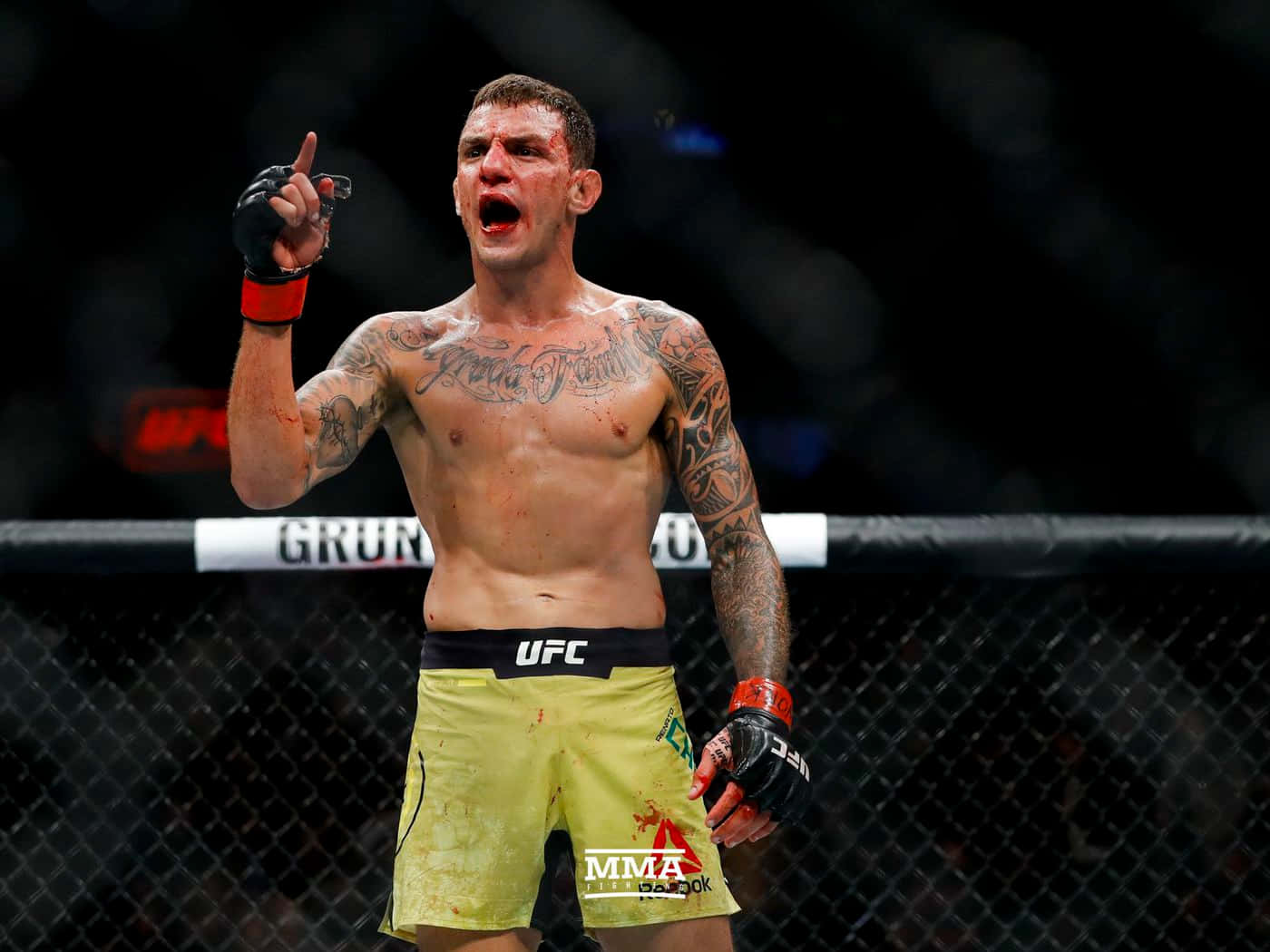MMA拳手在UFC八角籠內以血跡斑斑的身體和舉起的手指慶祝勝利。