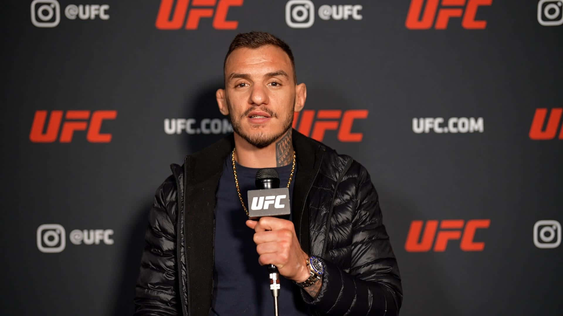 Renato Moicano 接受 UFC 專訪 壁紙 — 一名身穿黑色外套的男性拳手在記者會上，手持UFC麥克風，背景為品牌標誌。