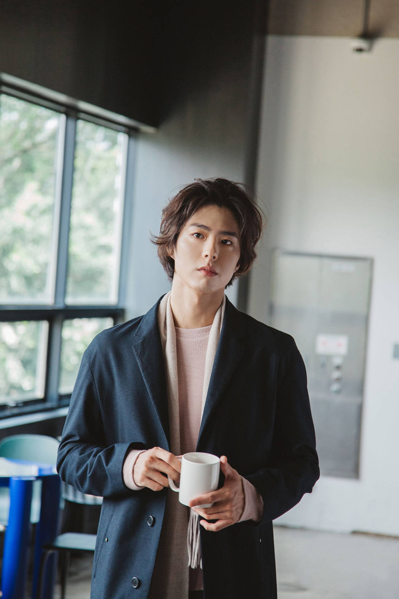 年輕男子穿外套在窗邊手持咖啡杯
