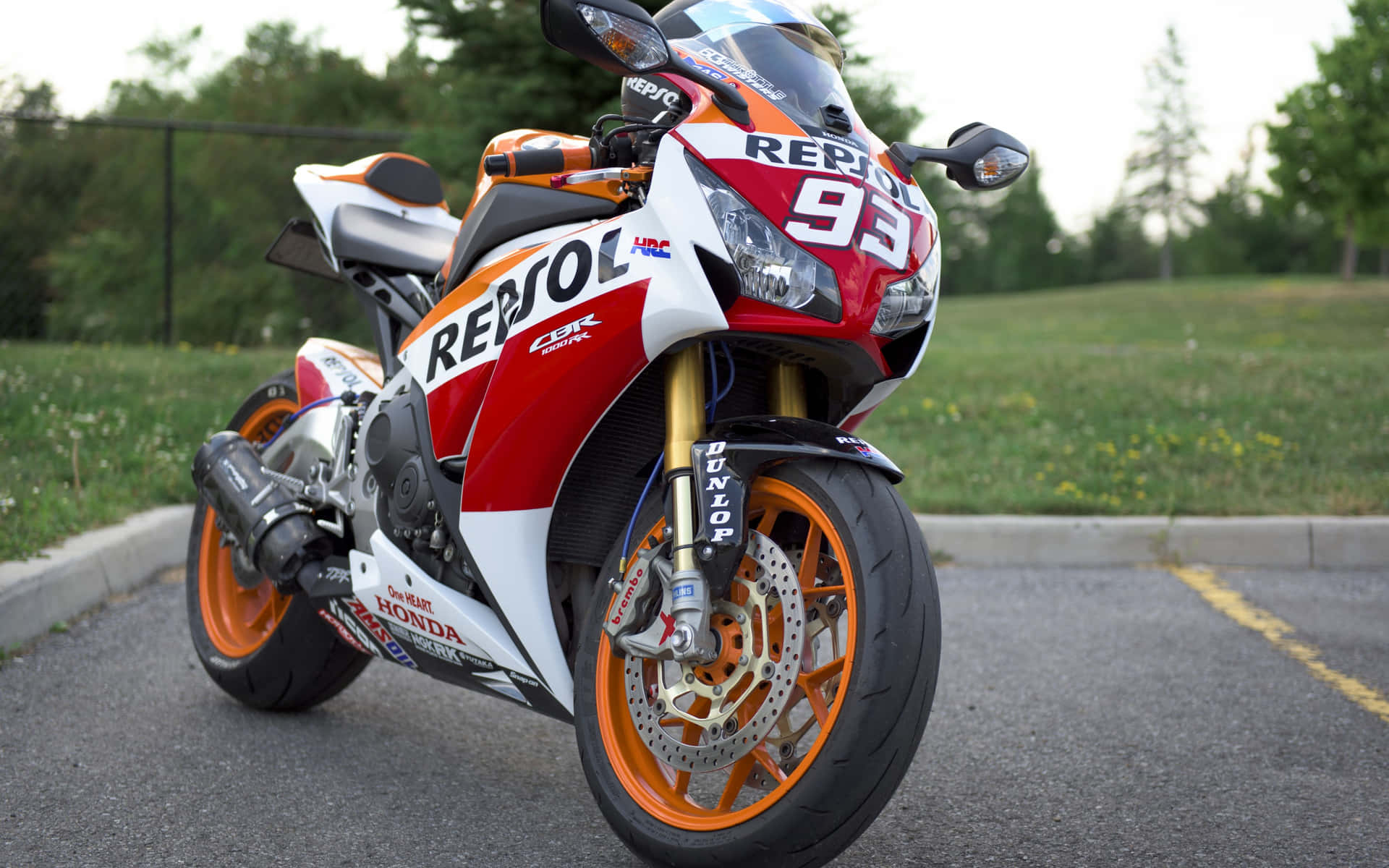 紅色、白色和橙色的Repsol Honda賽車電單車停在瀝青路上，靠近草地。