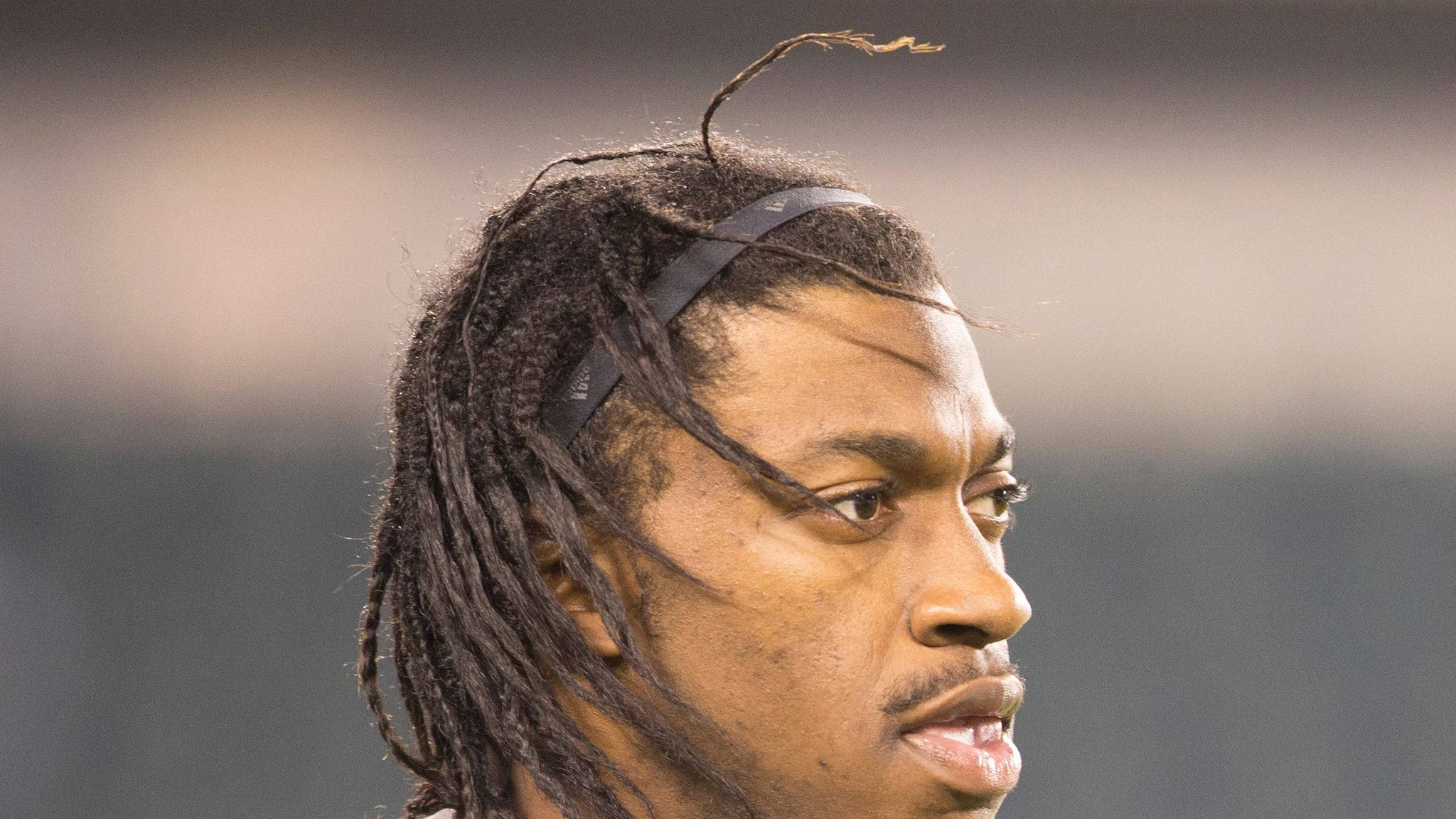 RG3 的 dreadlocks 壁紙 — 專注運動員的特寫，辮子頭髮和頭帶，背景是模糊的體育場。