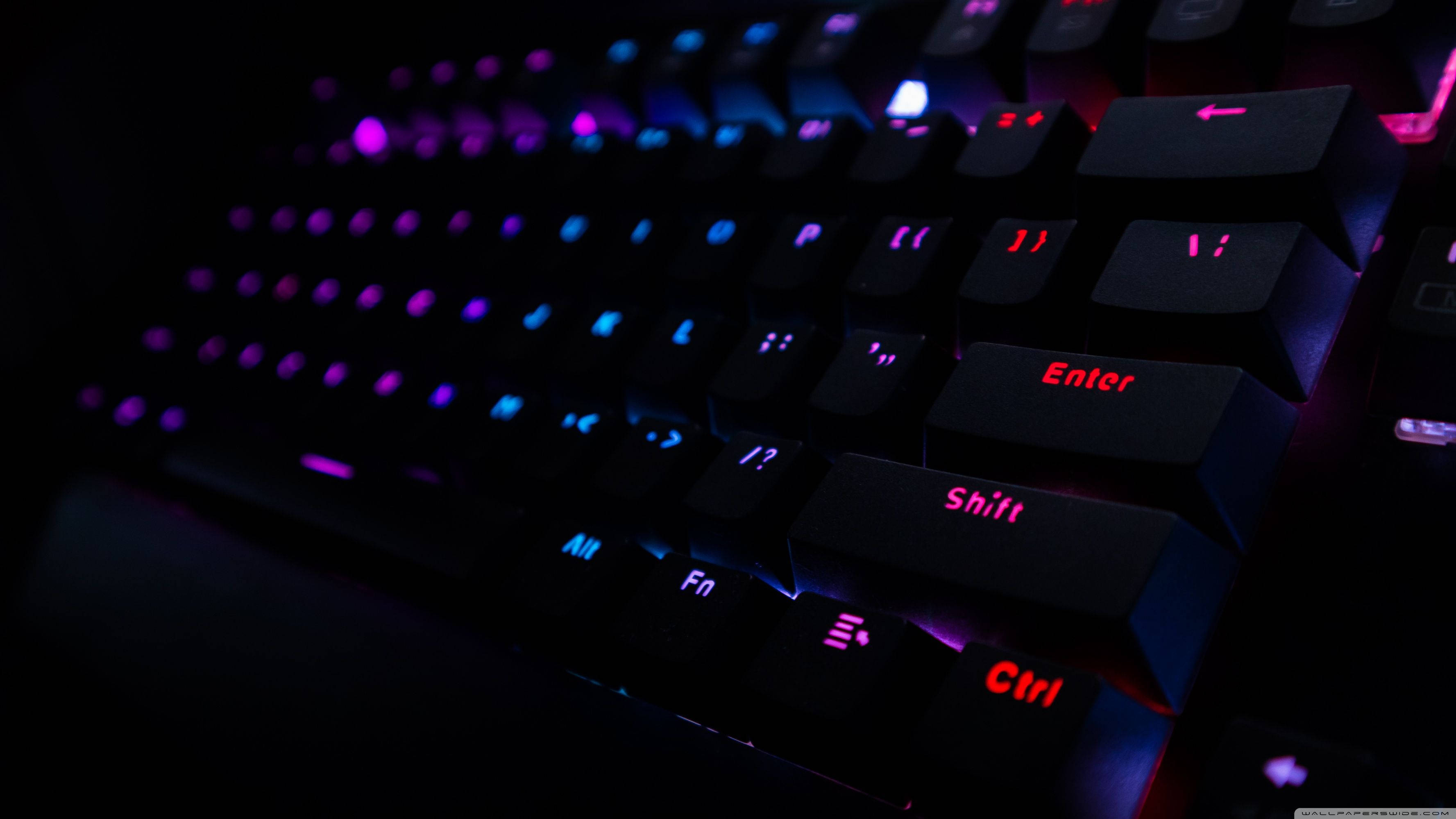 黑色鍵盤 RGB 4K 壁紙 — 黑色電競鍵盤在黑暗中發出鮮豔紫色和藍色背光的特寫。
