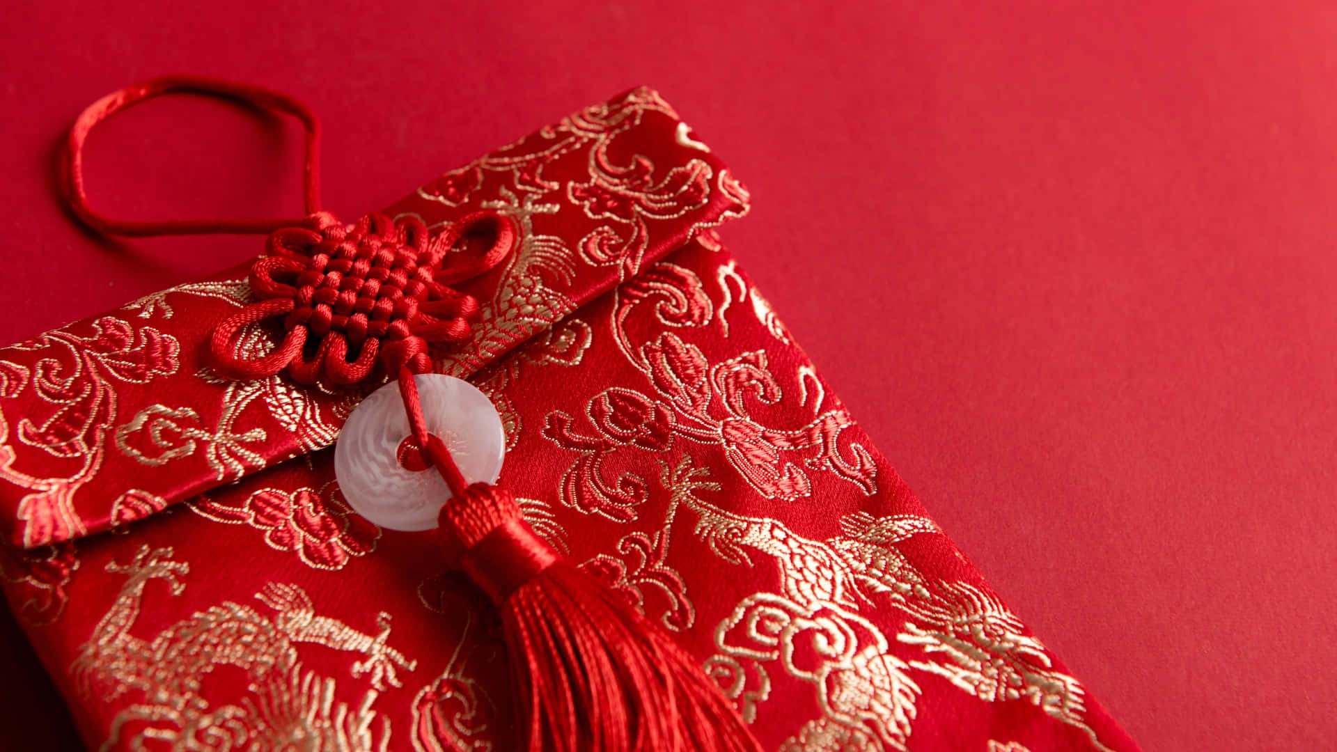  壁紙 — 一個帶有金龍刺繡和紅色結飾流蘇的豐盛紅色中式信封，放置在相配的紅色背景上。