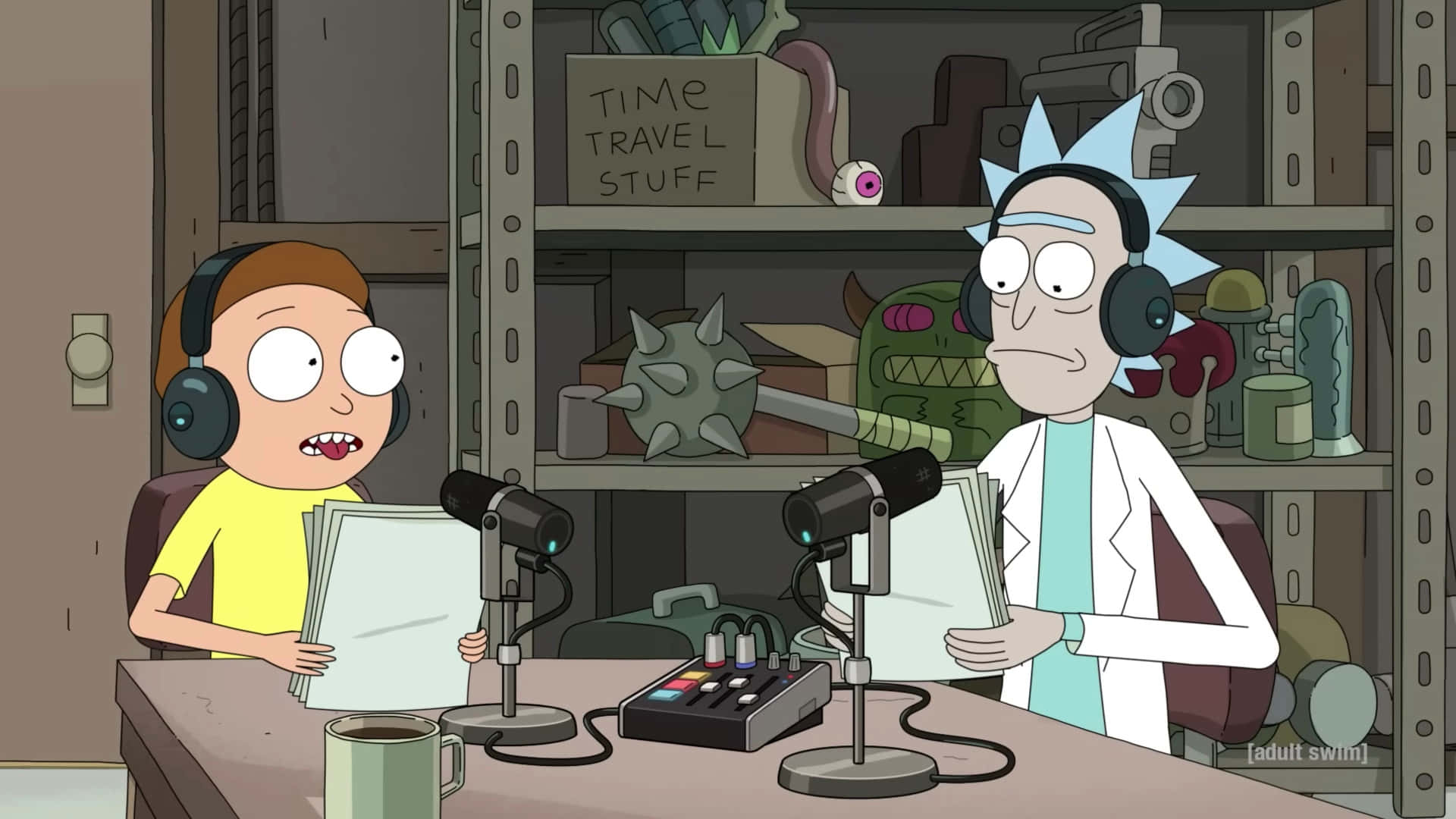 Rick And Morty 1920x1080 壁紙 — 喺昏暗嘅實驗室入面，Rick同Morty坐喺一個亂七八糟嘅枱前，枱上有咪高峰，周圍放滿奇怪嘅時間旅行文物。