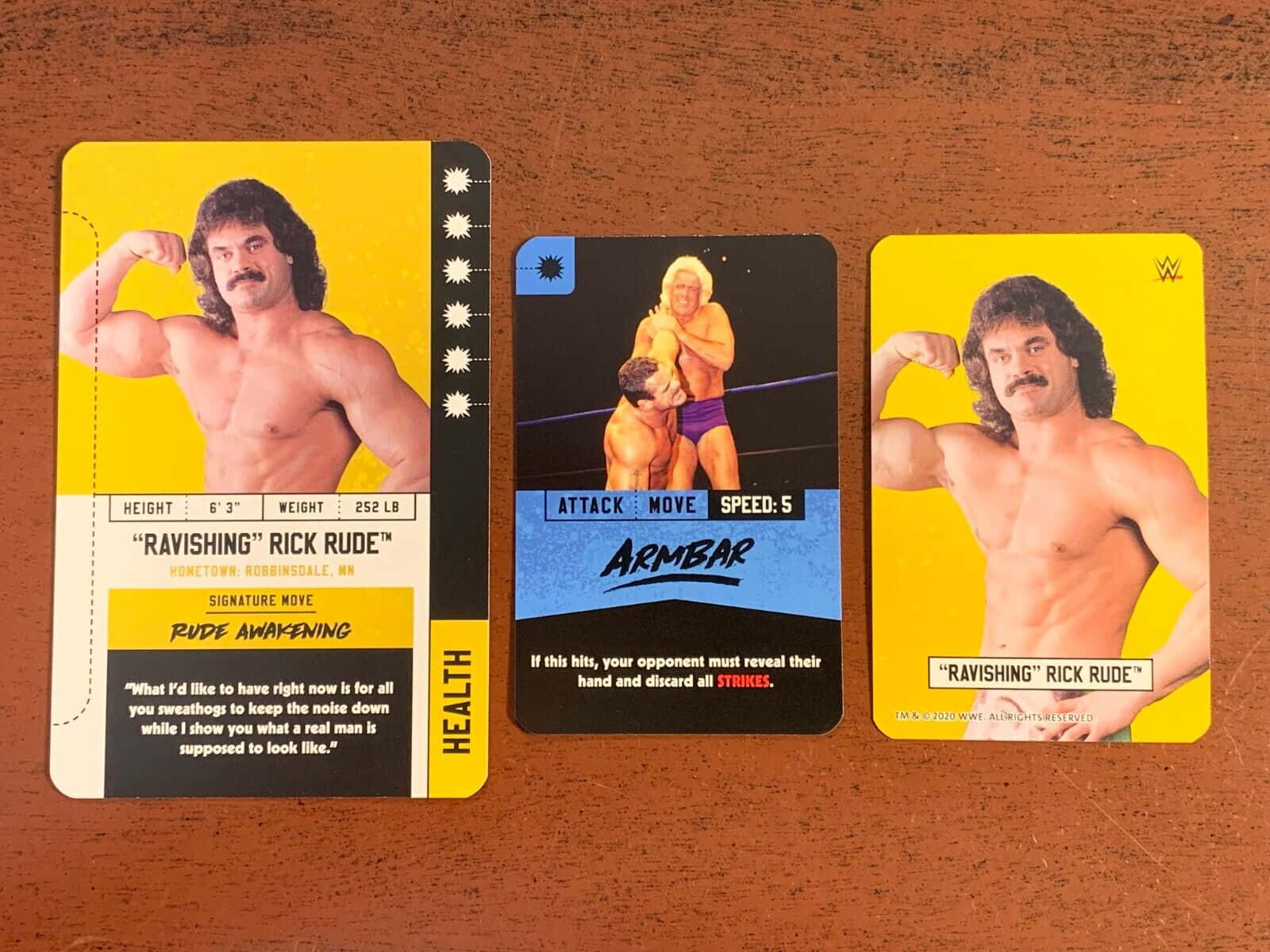 三張 Rick Rude 的 WWE 收藏卡放在木桌上。