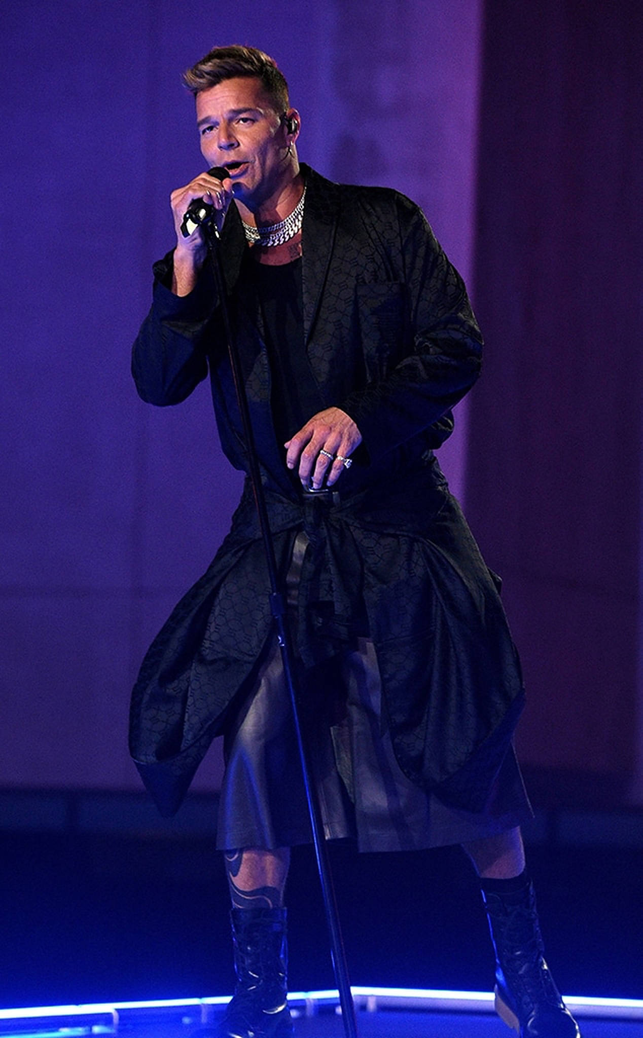 Ricky Martin 唱歌 壁紙 — 畢彼特在戲劇性的紫色和藍色燈光下，身穿黑色紋理長袍，在舞台上熱情表演。