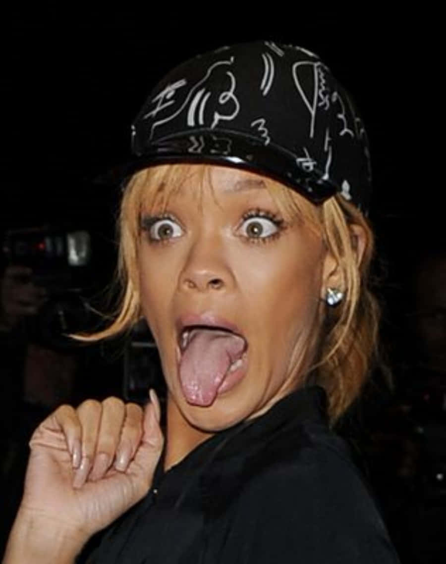 Celebrity Humor Memes 桌布 壁紙 — Rihanna 戴住黑色帽，上面有白色塗鴉圖案，俏皮咁伸出舌頭。