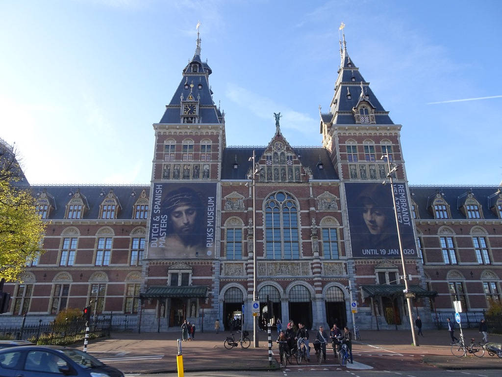 外牆展示名畫海報的 rijksmuseum 壁紙 — 阿姆斯特丹宏偉的紅磚國家博物館，裝飾華麗的塔樓和大型橫幅在清澈的藍天下。