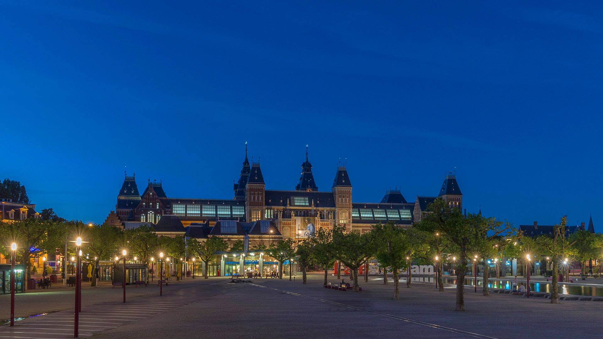 夜幕下藍天的 rijksmuseum 壁紙 — 宏偉的歷史建築，擁有發光的塔樓和拱形窗戶，在深藍色的暮色天空下巍然聳立。