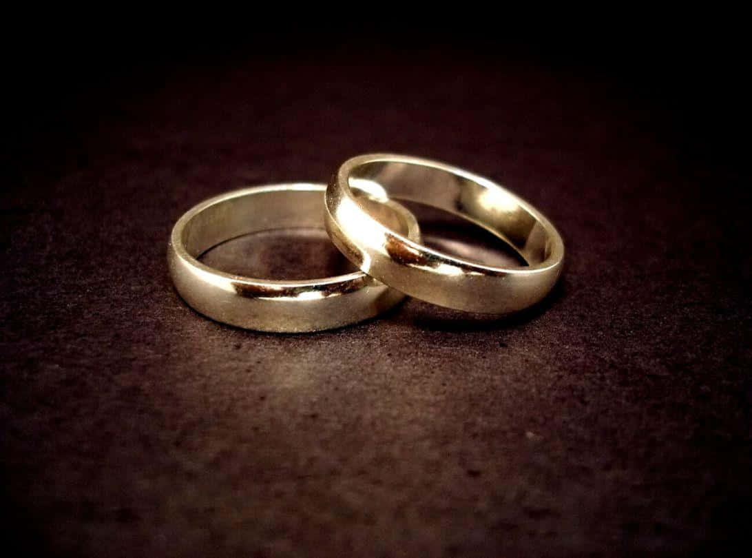 兩枚金色結婚戒指交纏在深色紋理表面上。