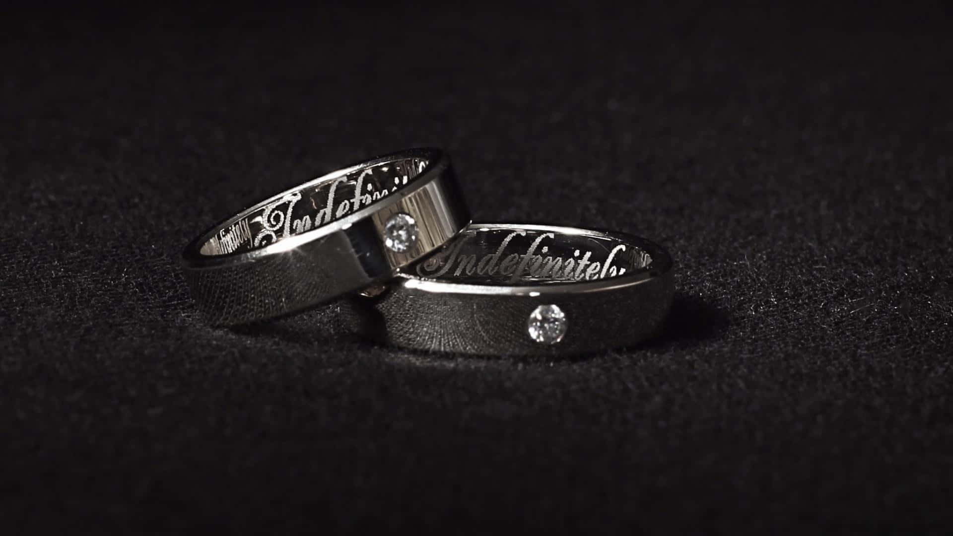 兩枚刻有字樣的結婚戒指，帶有鑽石，黑色背景。