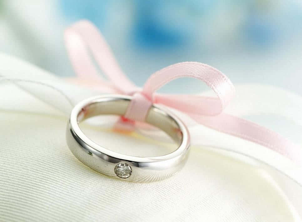 銀色結婚戒指，鑽石和粉紅色絲帶在白色布料上。
