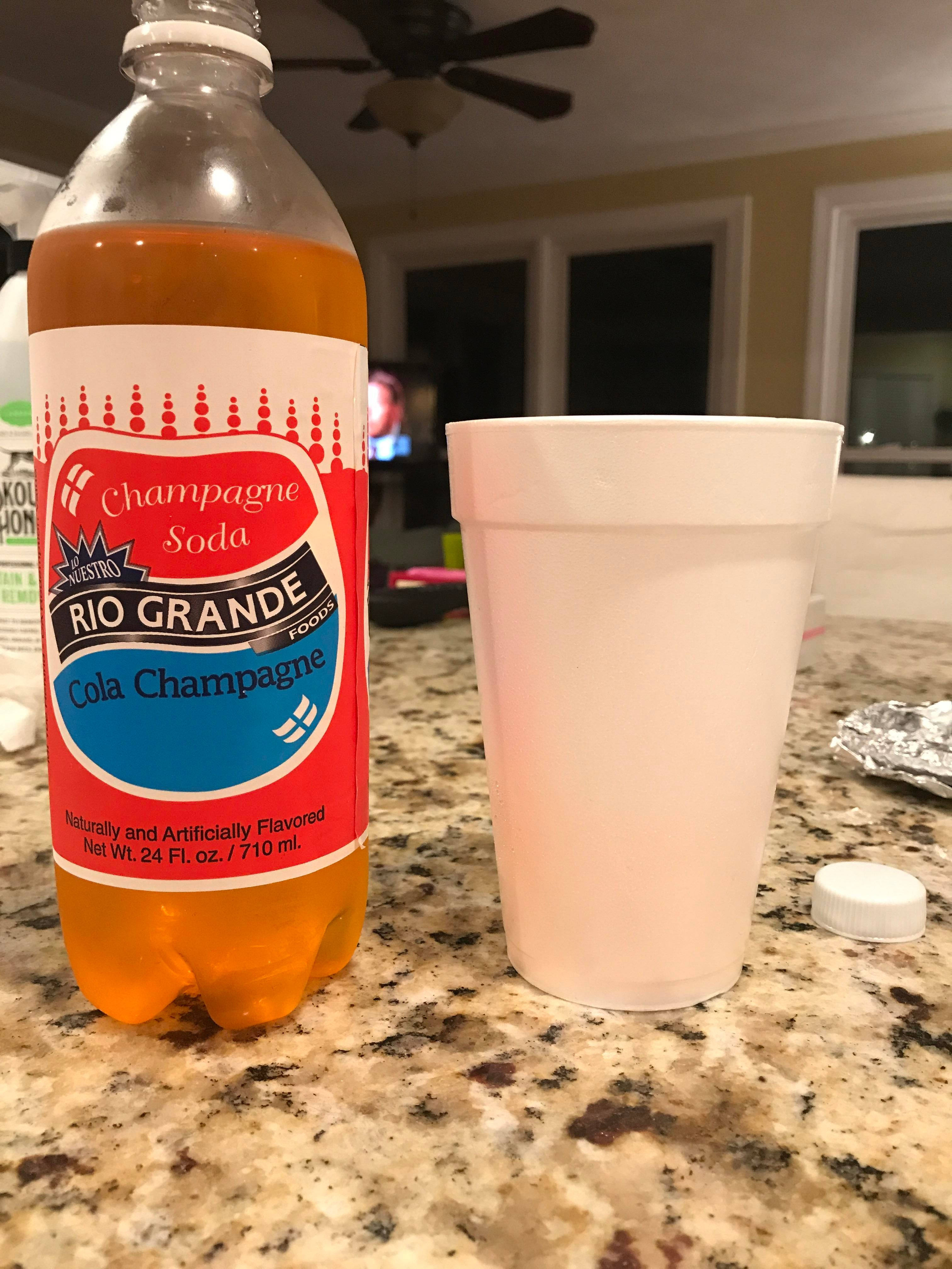 Rio Grande香檳汽水配杯 壁紙 — 一瓶Rio Grande Cola Champagne汽水放在一個有斑點的廚房檯面上，旁邊有一個白色發泡膠杯。