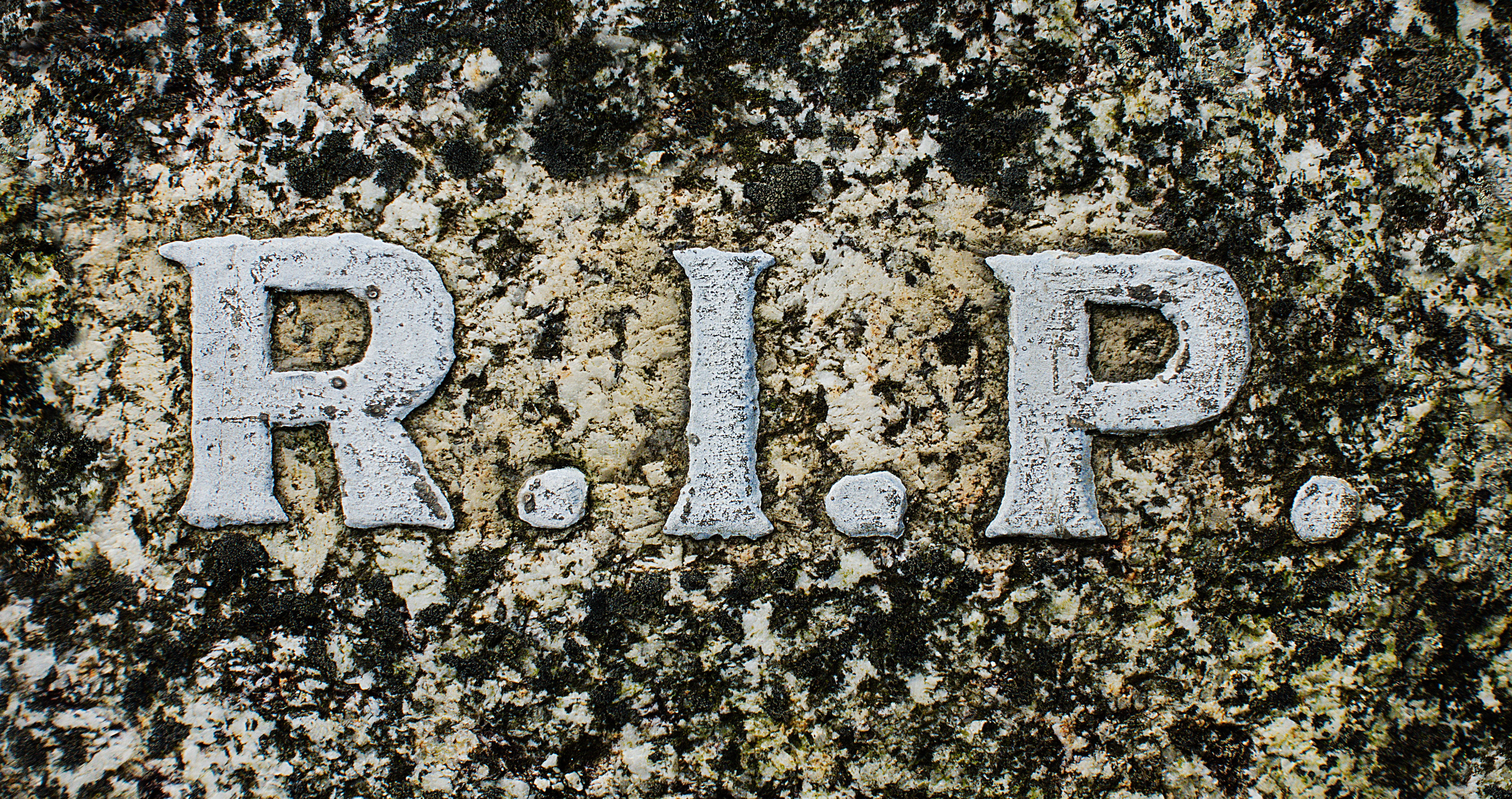 墓碑上的RIP字母特寫 壁紙 — 風化的白色字母拼出R.I.P.，嵌入在長滿苔蘚的花崗岩墓碑表面。