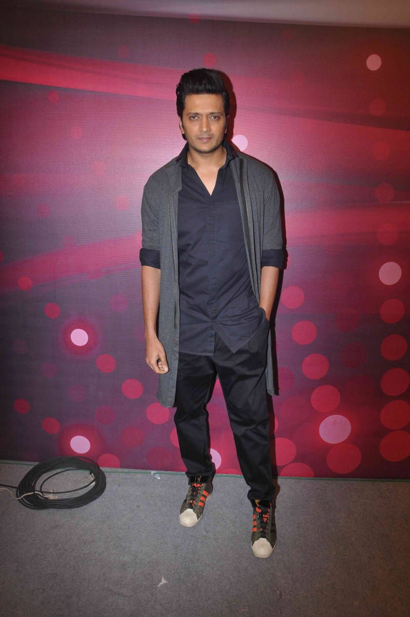 Riteish Deshmukh 身穿簡約黑色服裝 壁紙 — 一名身穿深色衣服的男子自信地站在充滿活力的紅色和紫色散景燈光背景前。