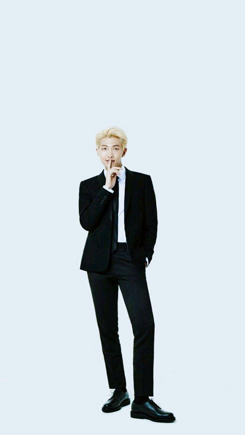 RM BTS《Lotte Duty Free》雜誌專屬壁紙 壁紙 — 一位時尚男士身穿黑色西裝，站在淺藍色背景前，將手指放在唇邊做出安靜的手勢。