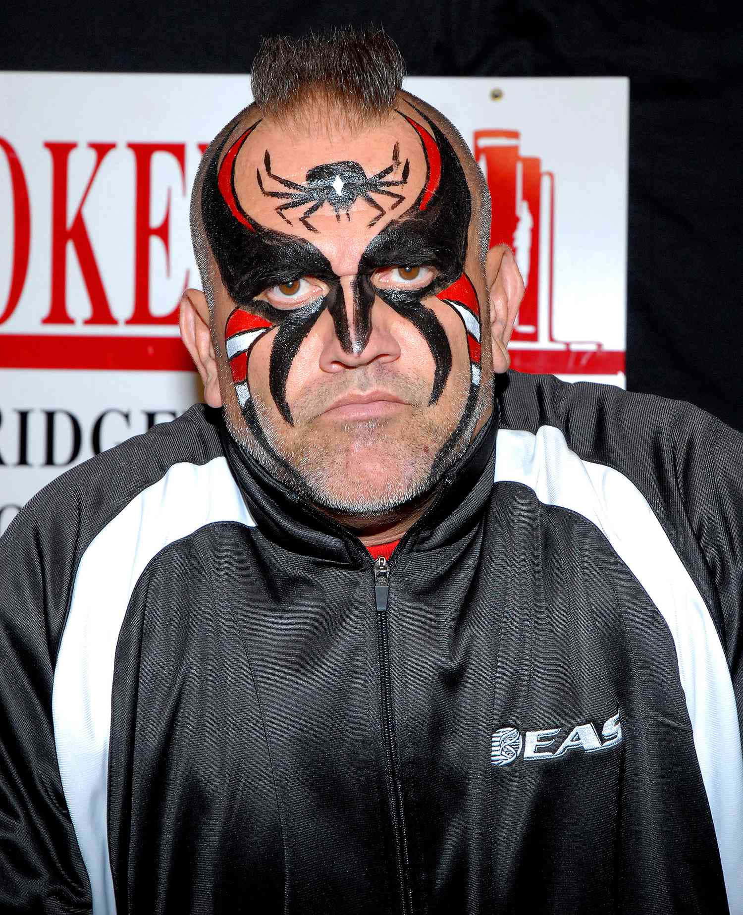 Road Warrior Hawk著名臉部塗裝 壁紙 — 一名摔角手臉上塗有黑、紅、白蜘蛛圖案，穿著黑白外套，專注地凝視鏡頭。