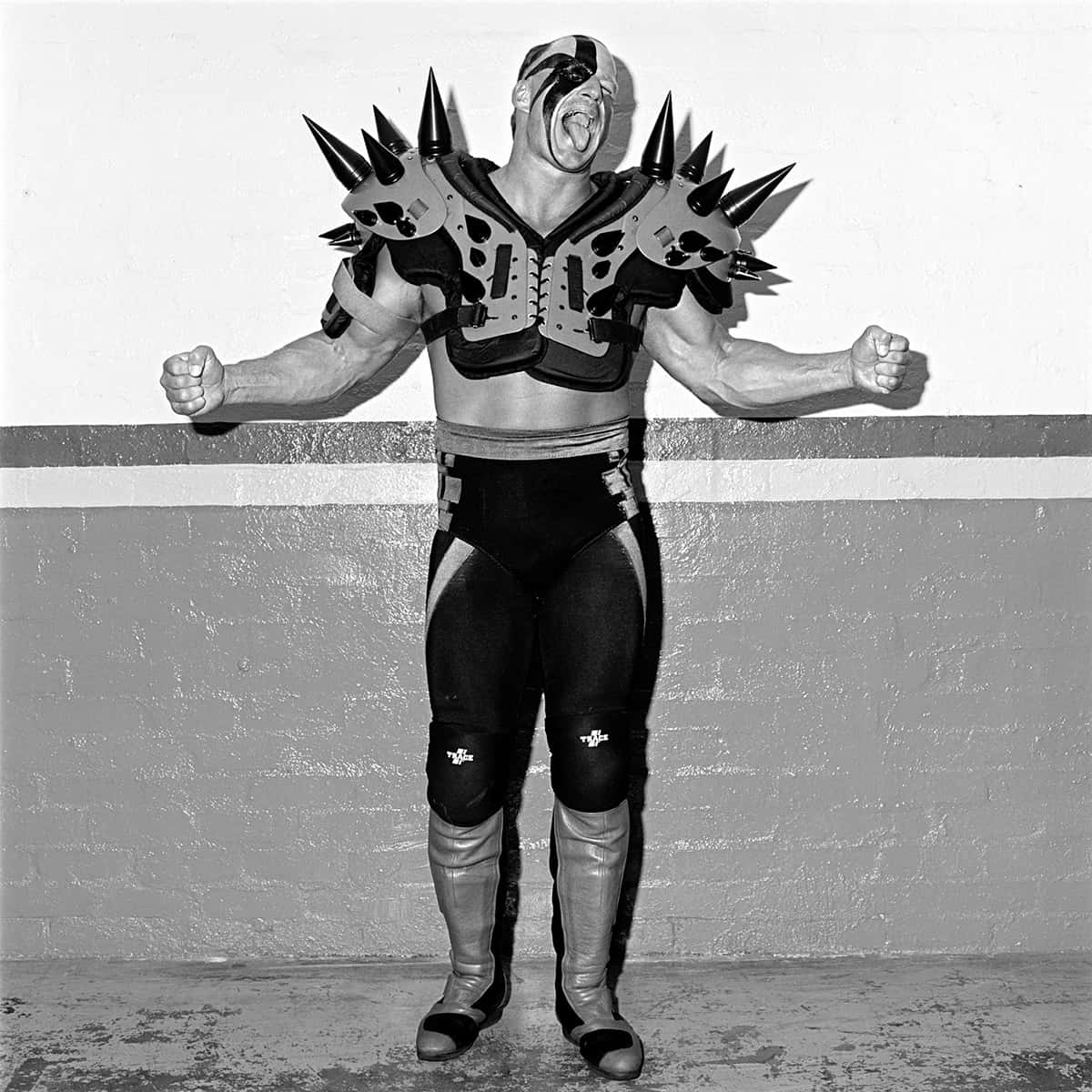 Road Warrior Hawk經典黑白舊照 壁紙 — 一個肌肉發達嘅摔角手，著住尖刺盔甲，握緊拳頭，對住普通牆壁咆哮，喺一張粗糙嘅黑白相入面。