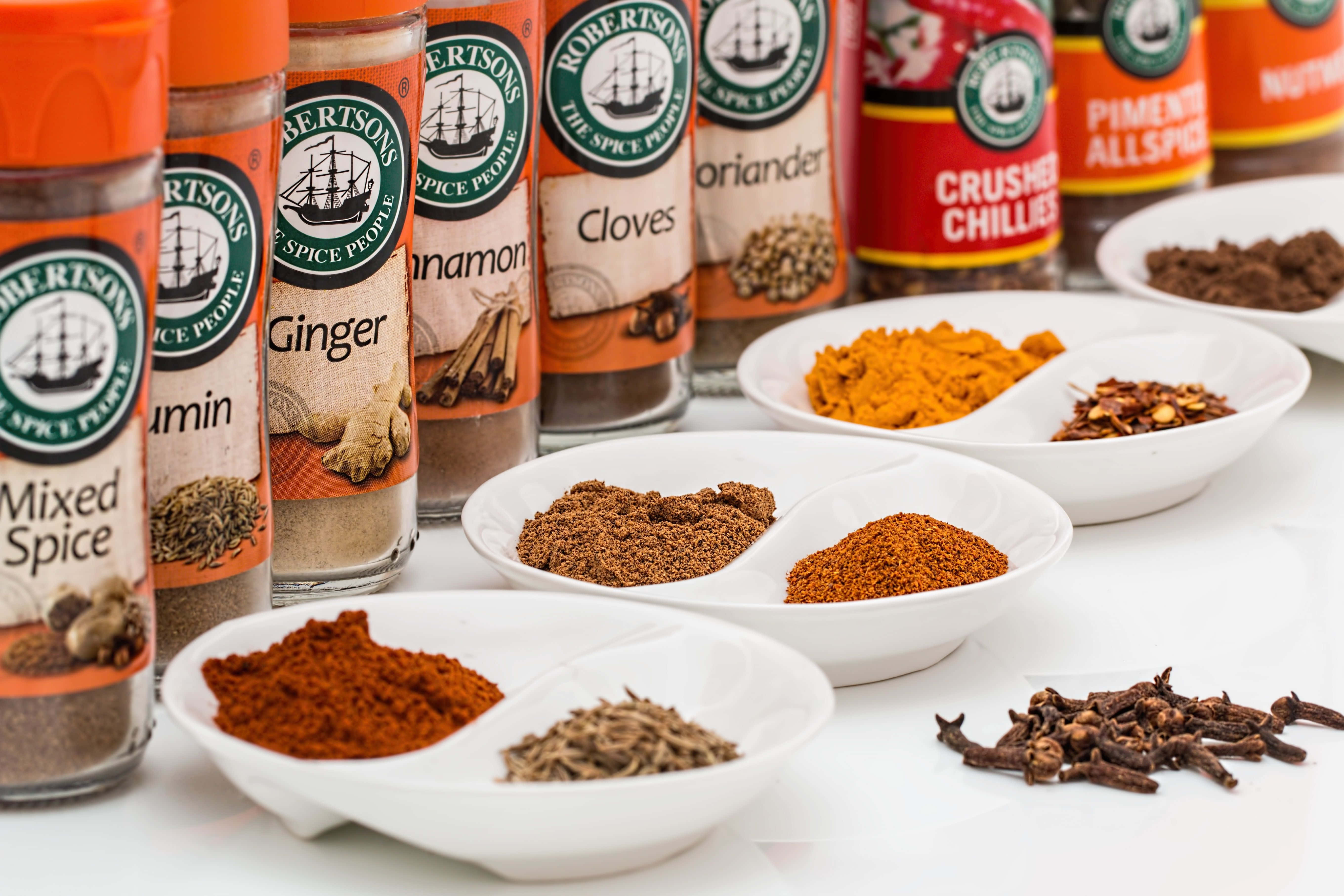 Spices 桌布 壁紙 — Robertson's 香料瓶和碗中裝滿了色彩繽紛的研磨香料，如肉桂、生薑和辣椒，整齊地排列在白色表面上。