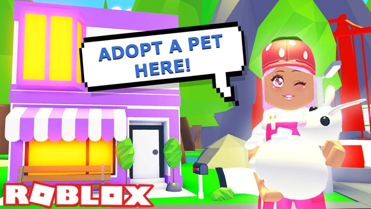 Roblox Adopt Me 意大利麵店 壁紙 — 一個粉紅色頭髮、戴紅色帽子的Roblox角色，喺一間色彩繽紛嘅寵物店前面抱住一隻白色兔仔，舖頭嘅招牌寫住adopt a pet here！
