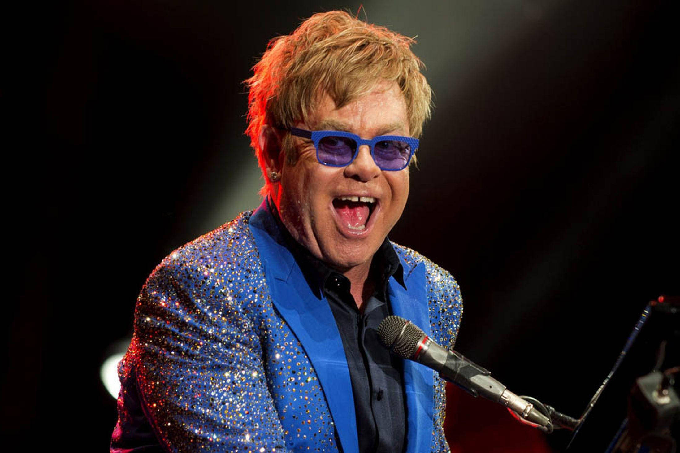 Rocketman 微笑演唱 壁紙 — 艾頓莊在舞台燈光下穿著閃閃發光的藍色外套熱情地唱歌。